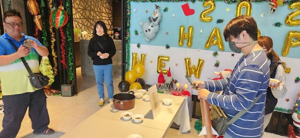 新年派對上的人們。氣球上寫著「2023年新年快樂」。人們圍坐在桌旁,有些人手裡拿著東西。
