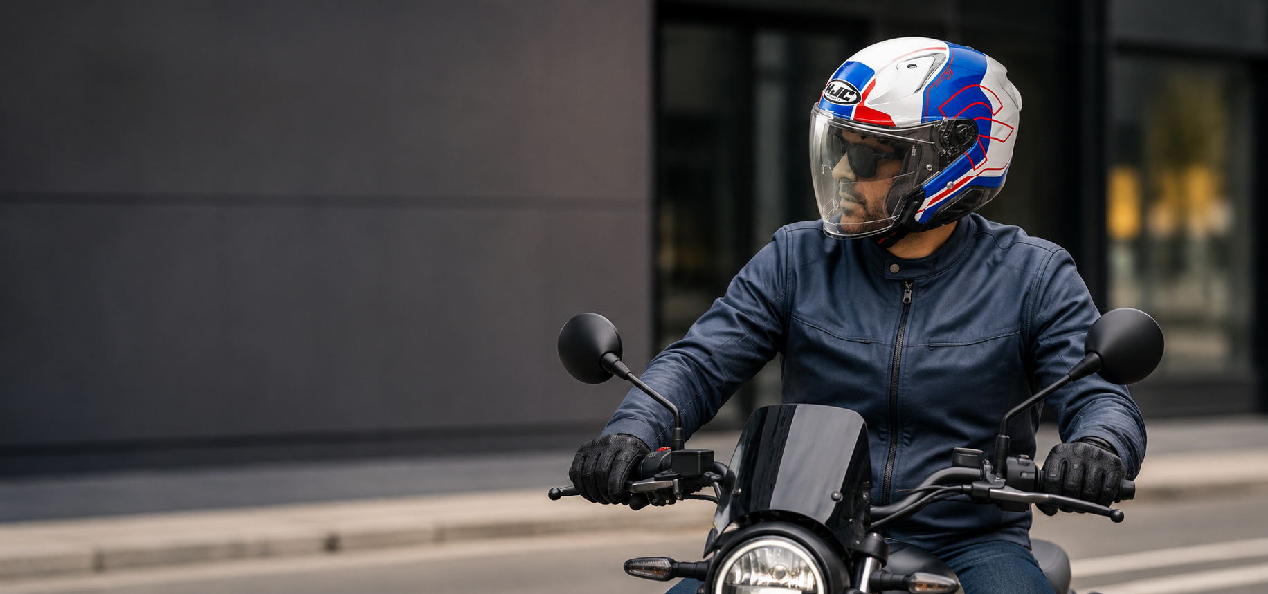 Un motociclista con giacca blu e casco guida uno scooter su una strada cittadina.