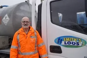 Man in orange jacket stands beside a truck with 