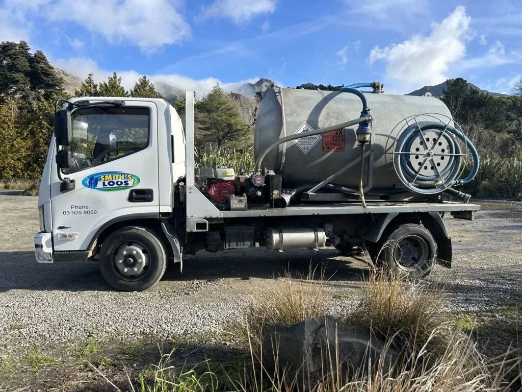 White truck with large tank, hose reel, and mountains in the background.