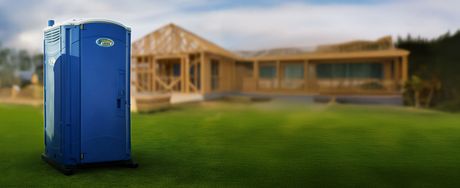 Blue portable toilet on a green lawn with a house under construction in the background.