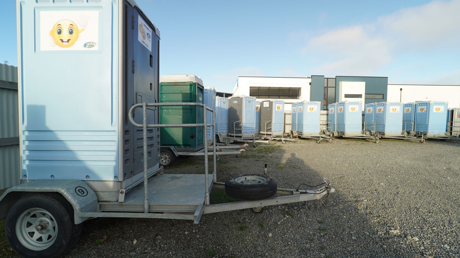 Blue portable toilets on trailers parked outdoors, under a clear sky.