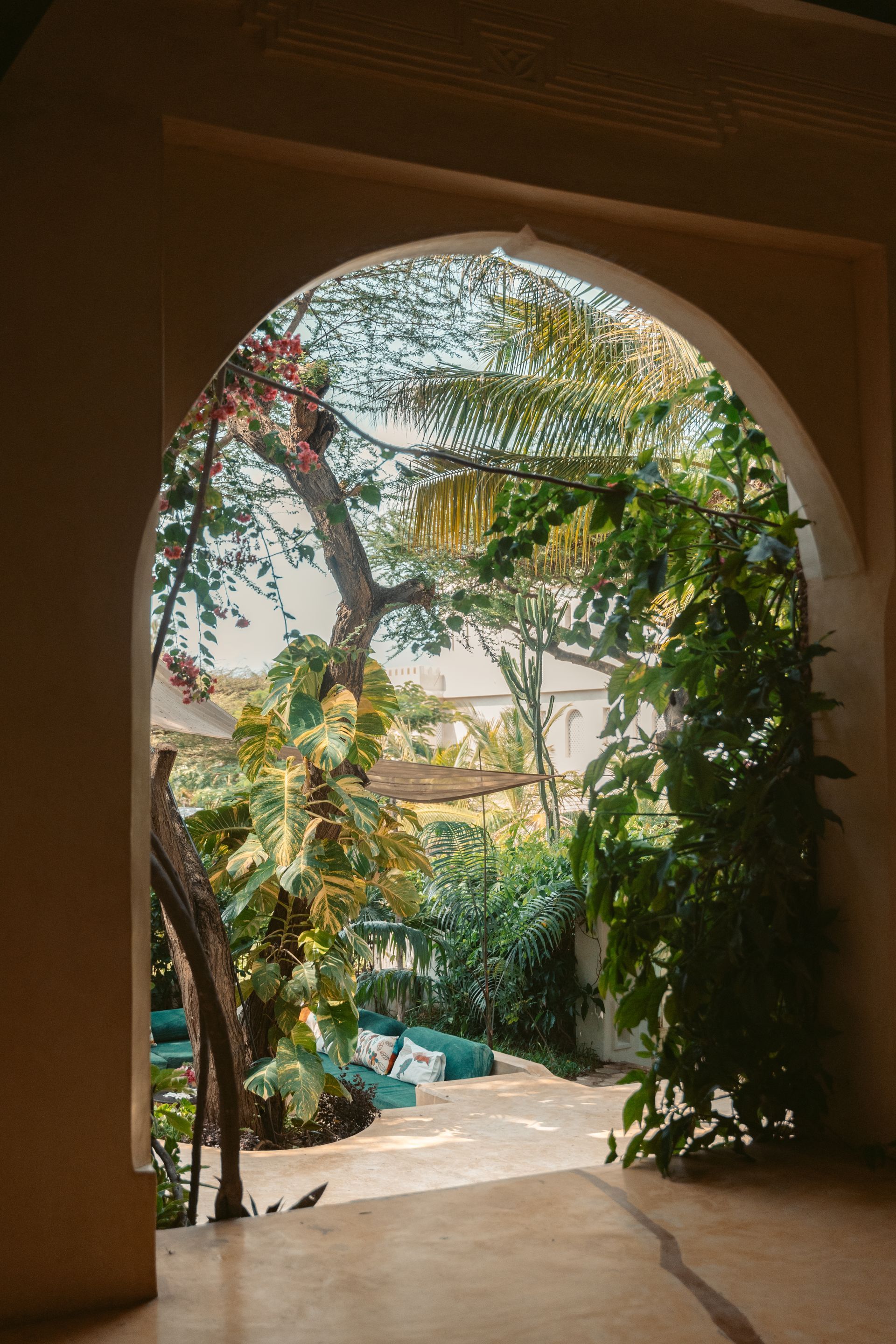 Swahili arch opening to a peaceful balcony view of garden with palm leaves and flowers