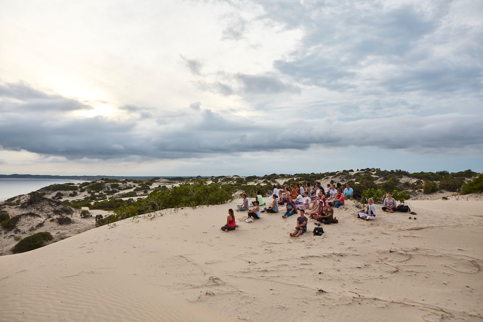 Wellness retreat participants sitting together on scenic sand dunes overlooking the Indian Ocean in Lamu during a Banana House wellness retreat.