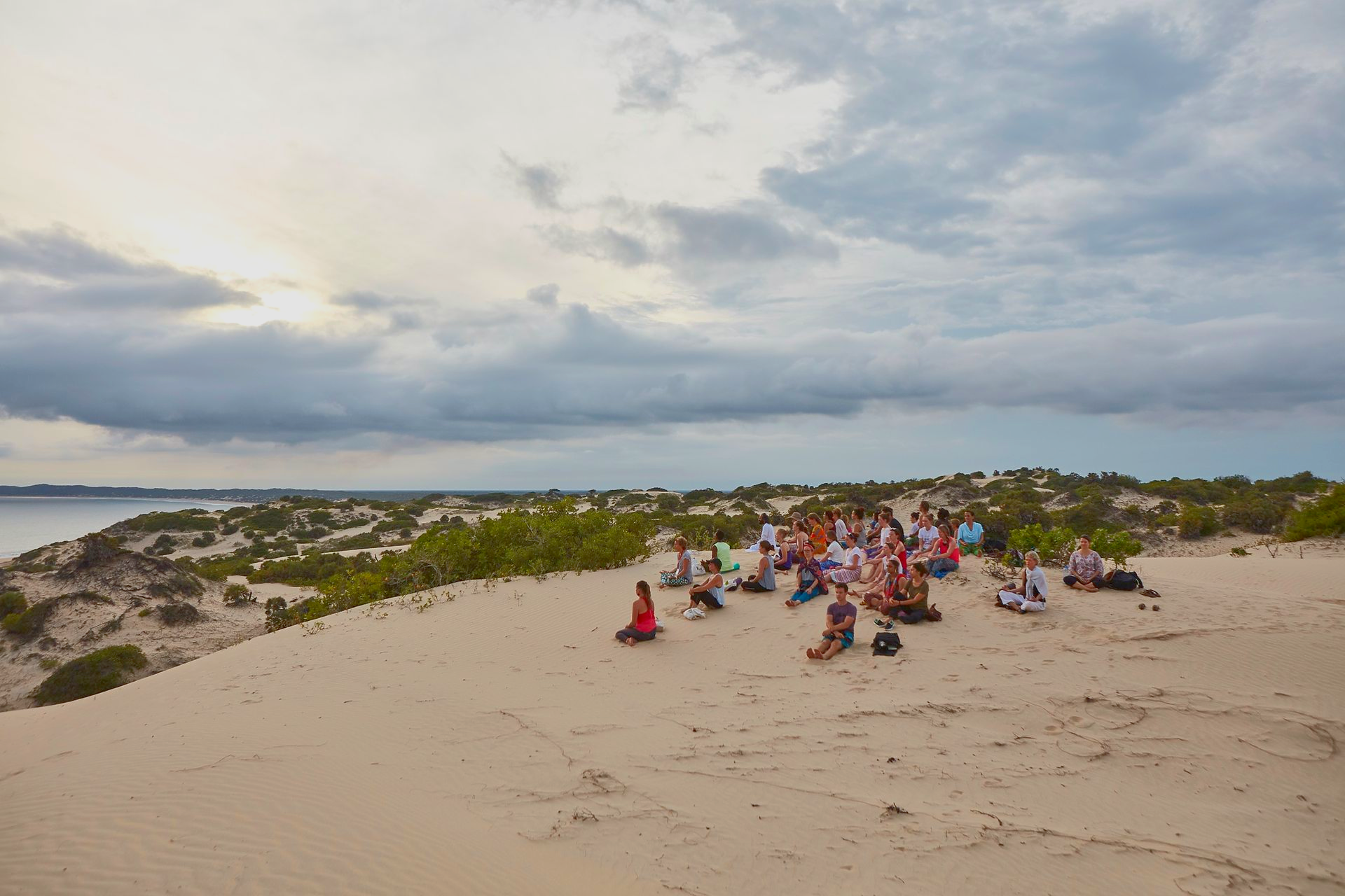 Wellness retreat participants sitting together on scenic sand dunes overlooking the  Ocean in Lamu during a Banana House wellness retreat.