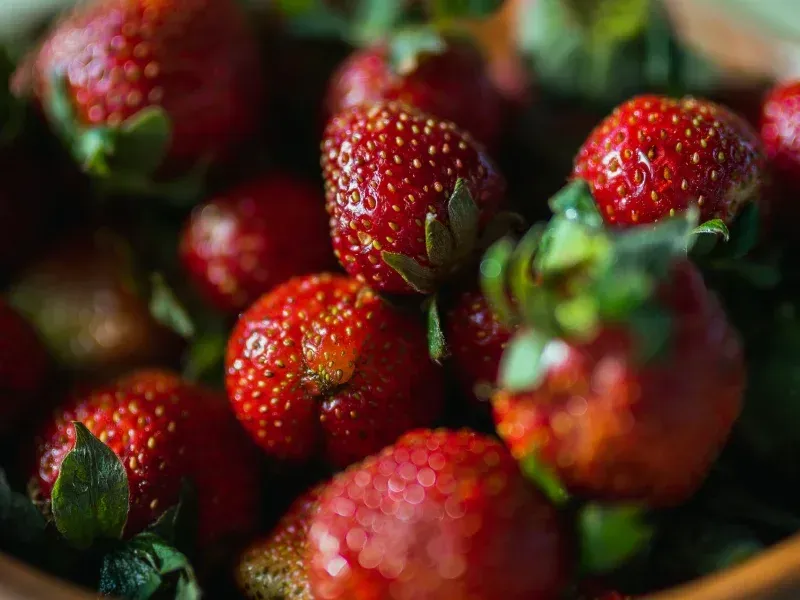 Close-up of ripe red strawberries with green leaves, gathered in a bowl.