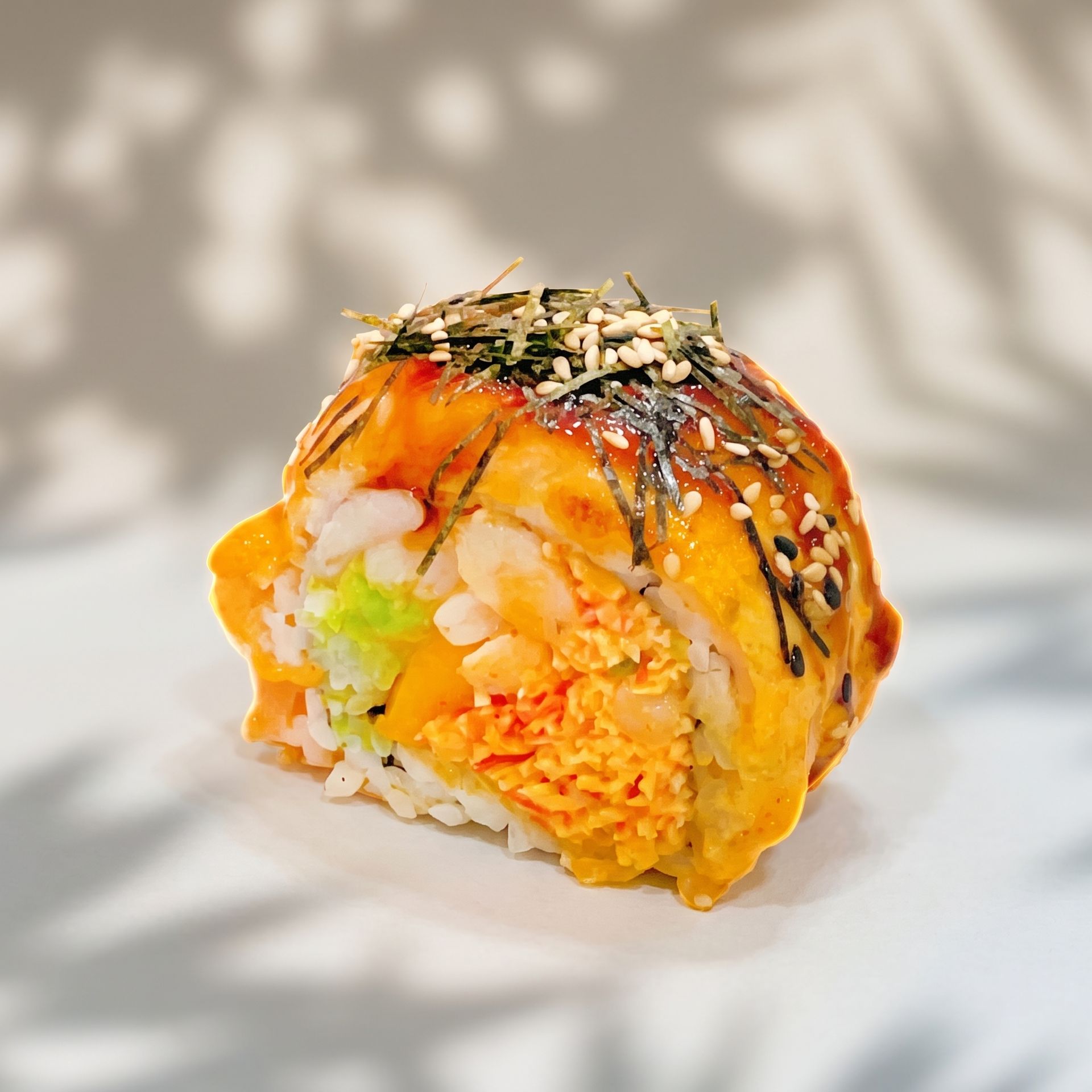 Close-up of a colorful sushi roll with orange sauce and sesame seeds on a light background