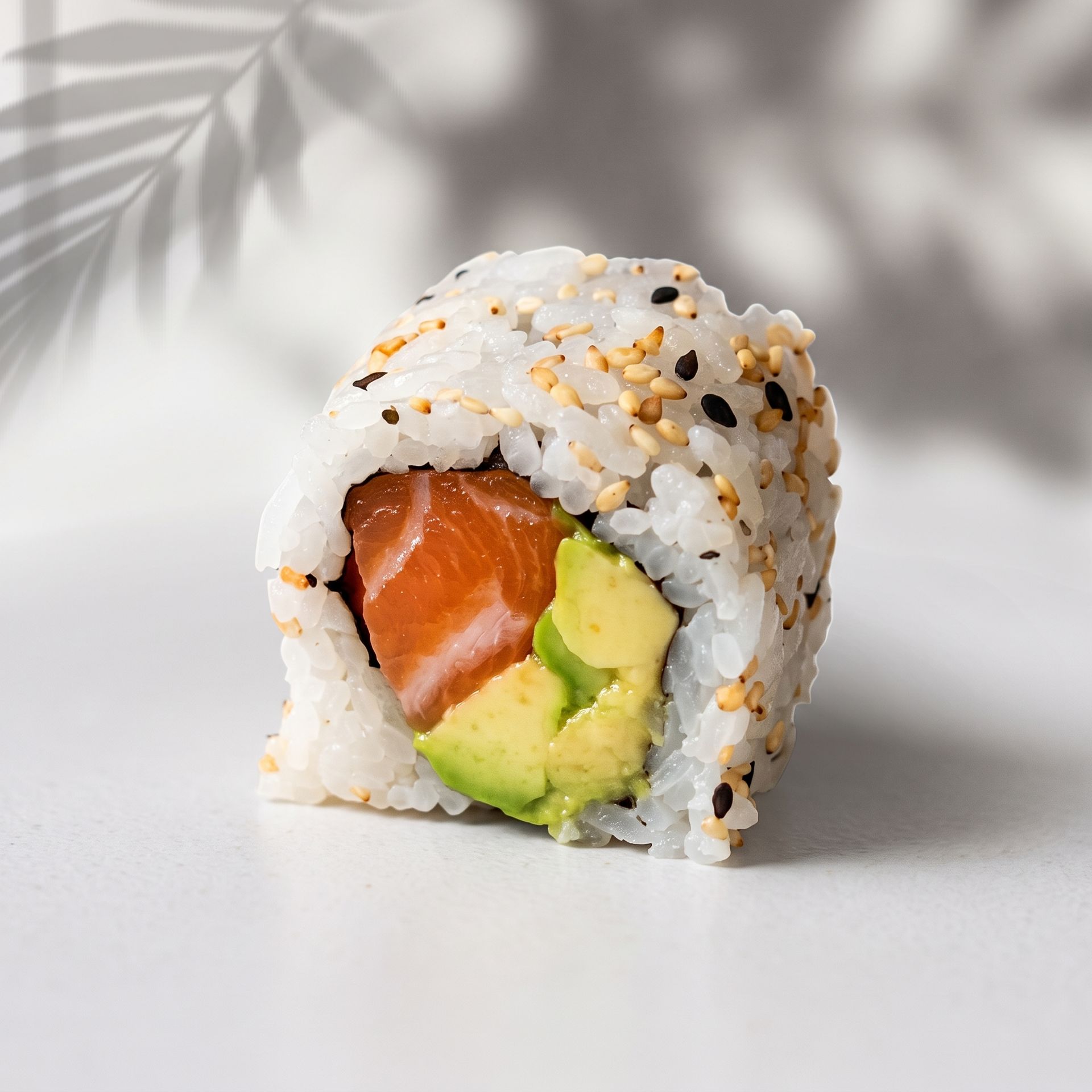 Close-up of a sushi roll with salmon, avocado, and sesame seeds on a light background