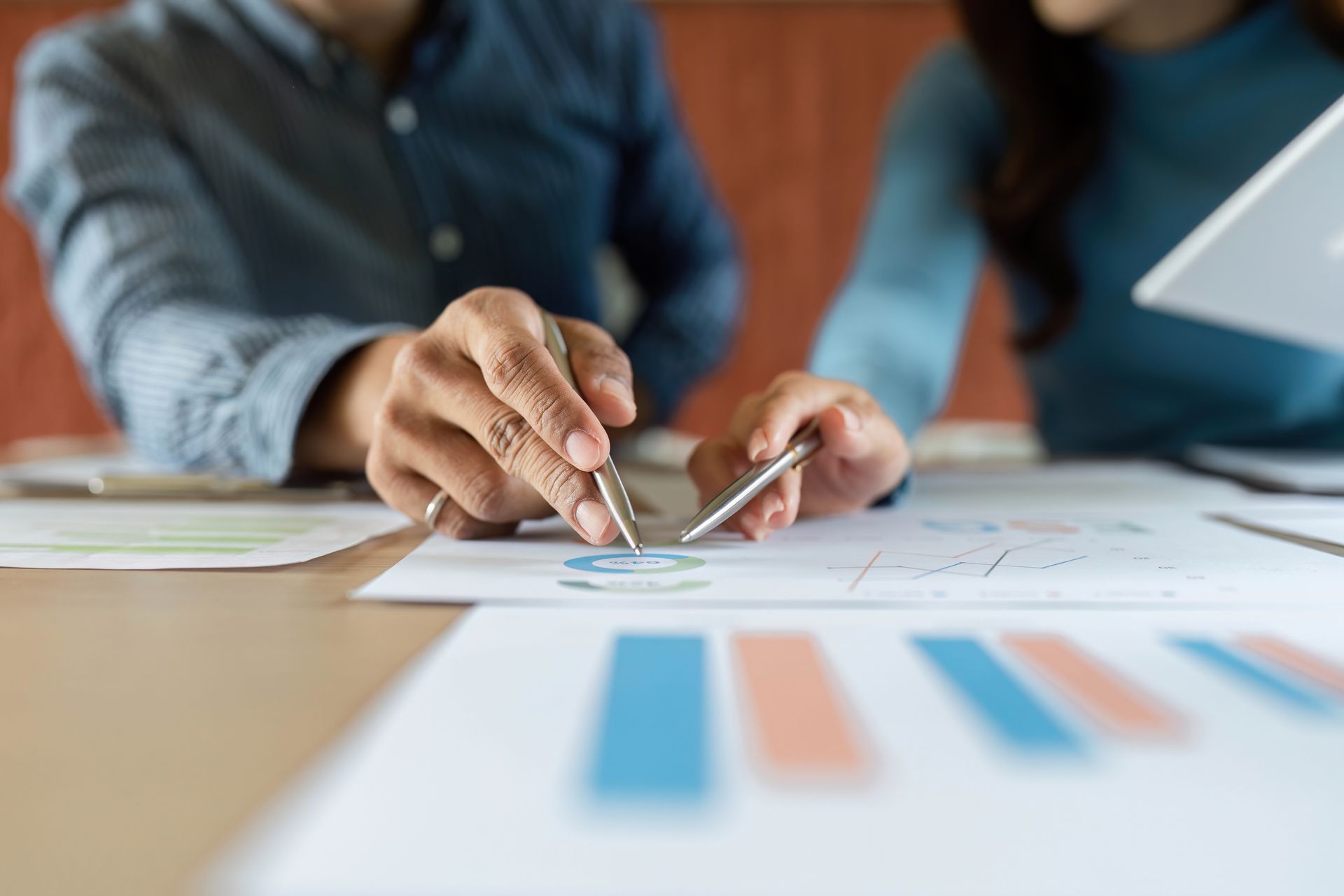 Hands adjusting a metal compass over blueprints beside a blurred bar chart on a desk