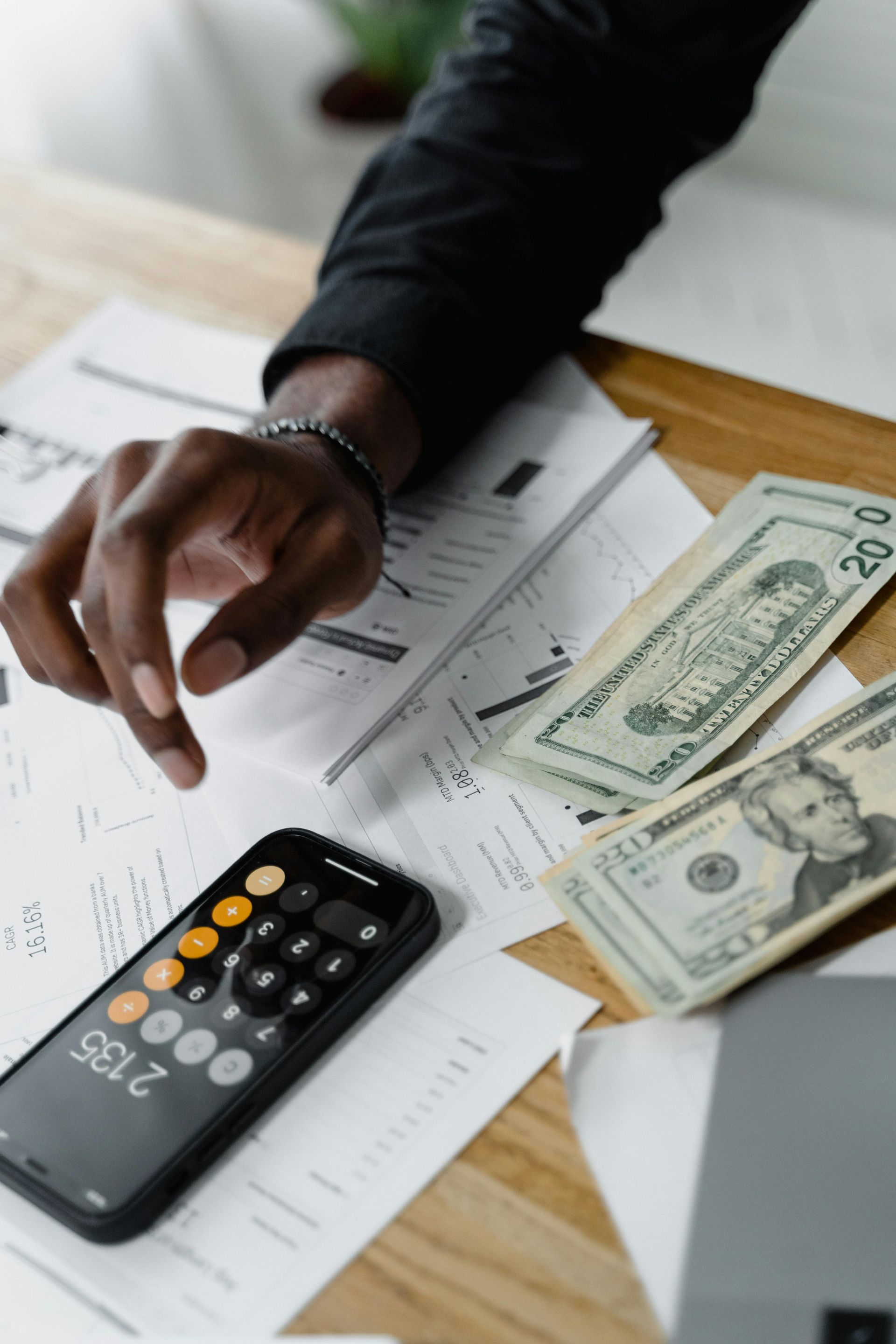 Two professionals in business suits shake hands over a table covered with financial charts and documents.