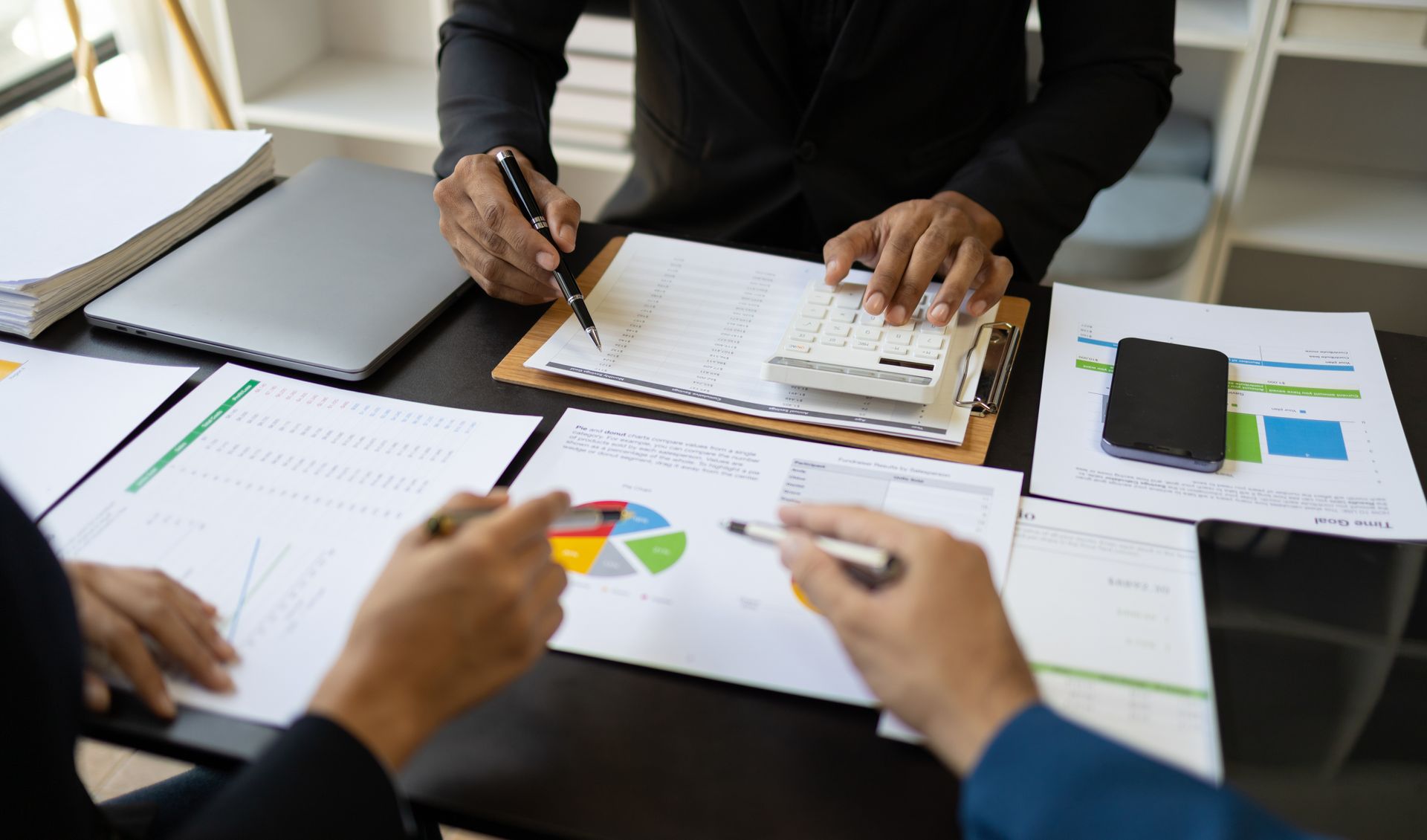 People collaborating at a desk with charts, notebooks, and a smartphone during a meeting