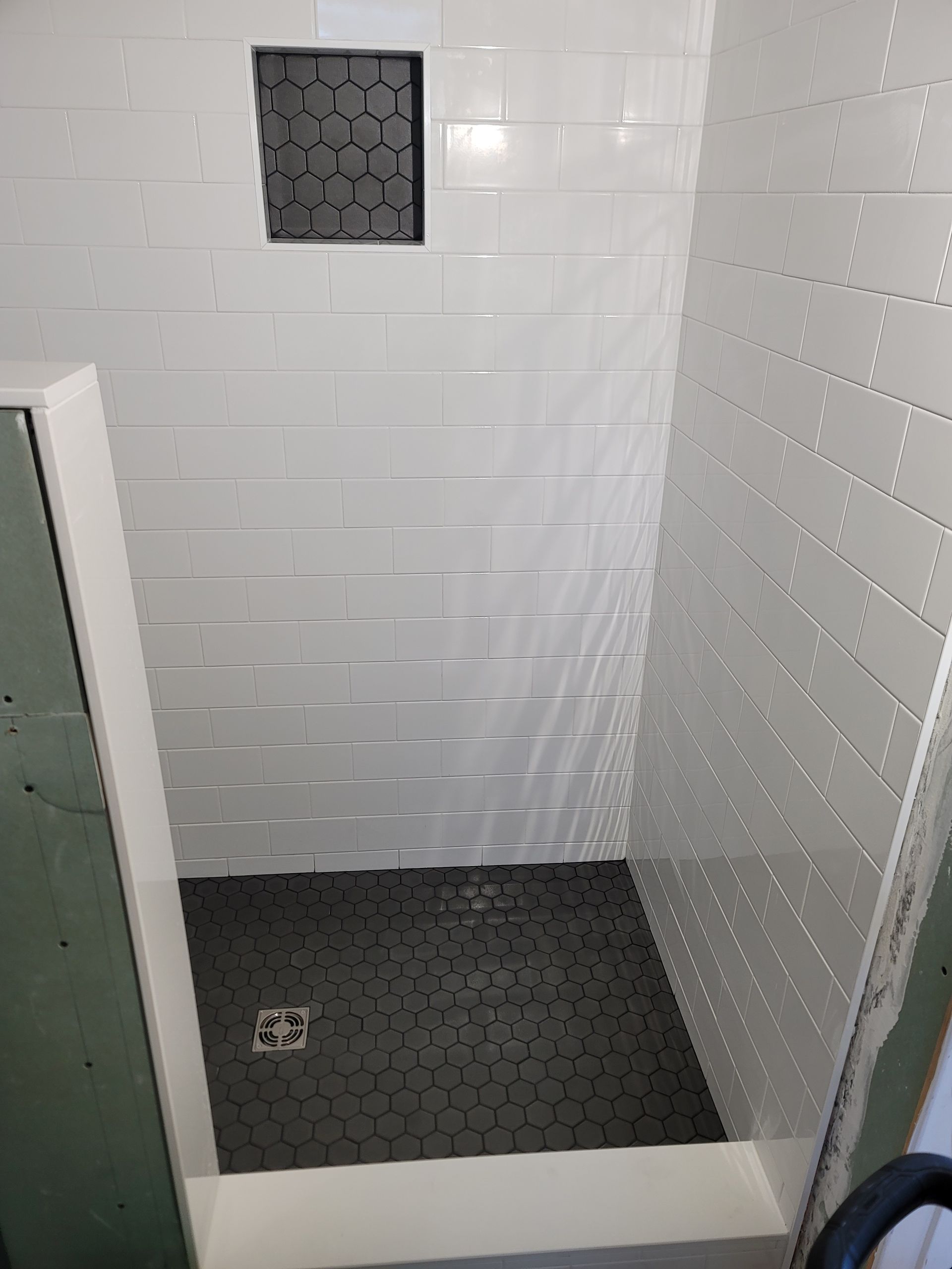 Small white-tiled shower stall with black hexagonal floor and a square wall niche.