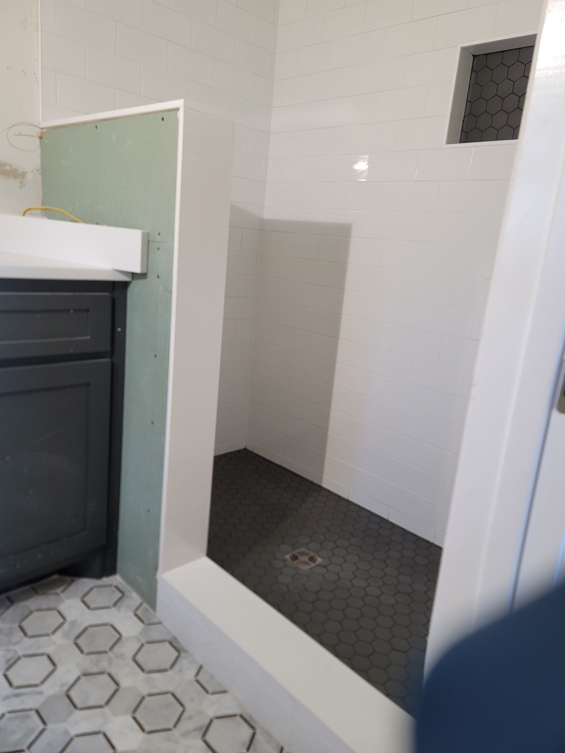Small tiled shower stall with white walls and dark floor in a bathroom