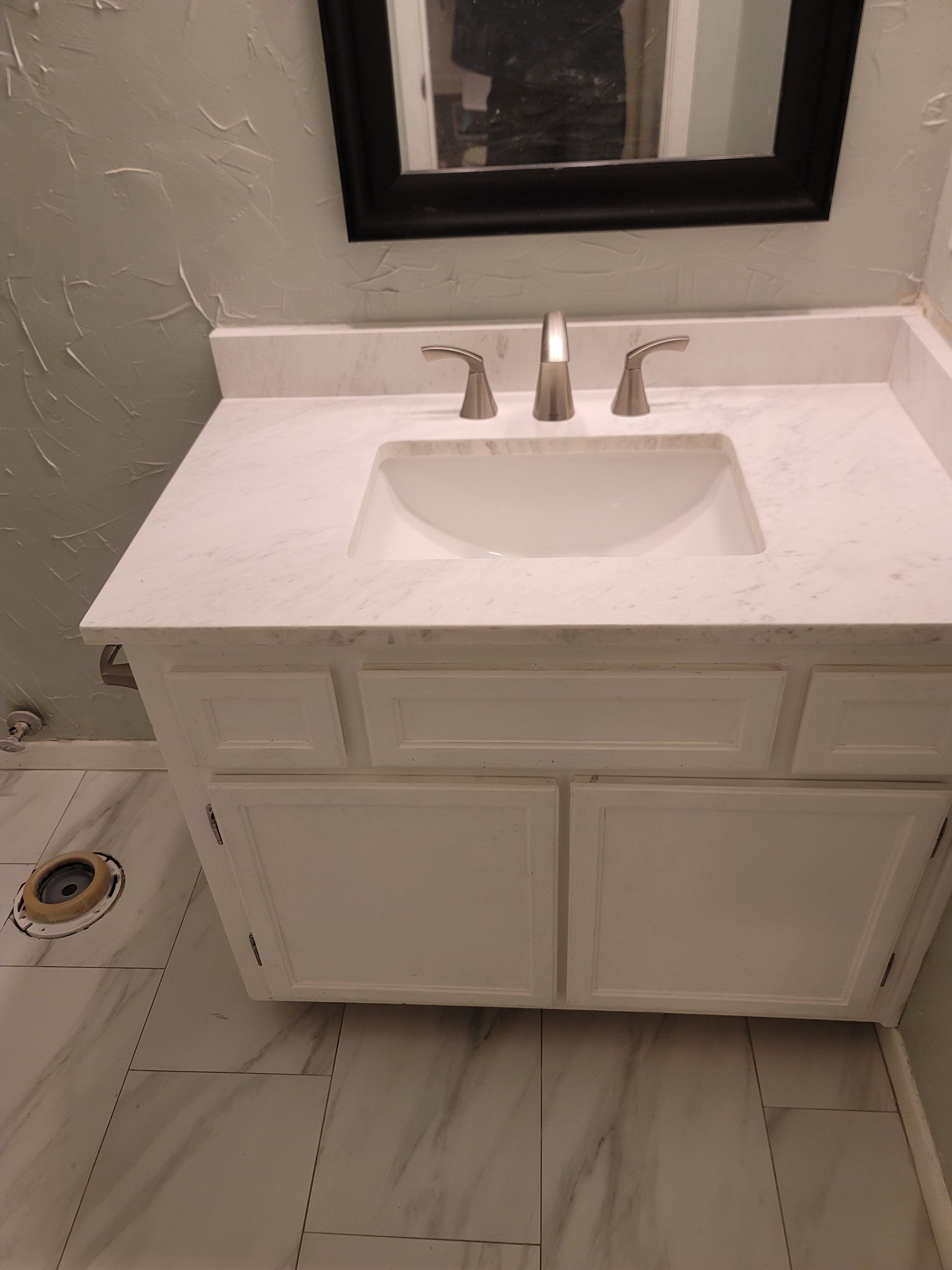White bathroom vanity with sink and mirror beside a toilet in a small tiled bathroom.
