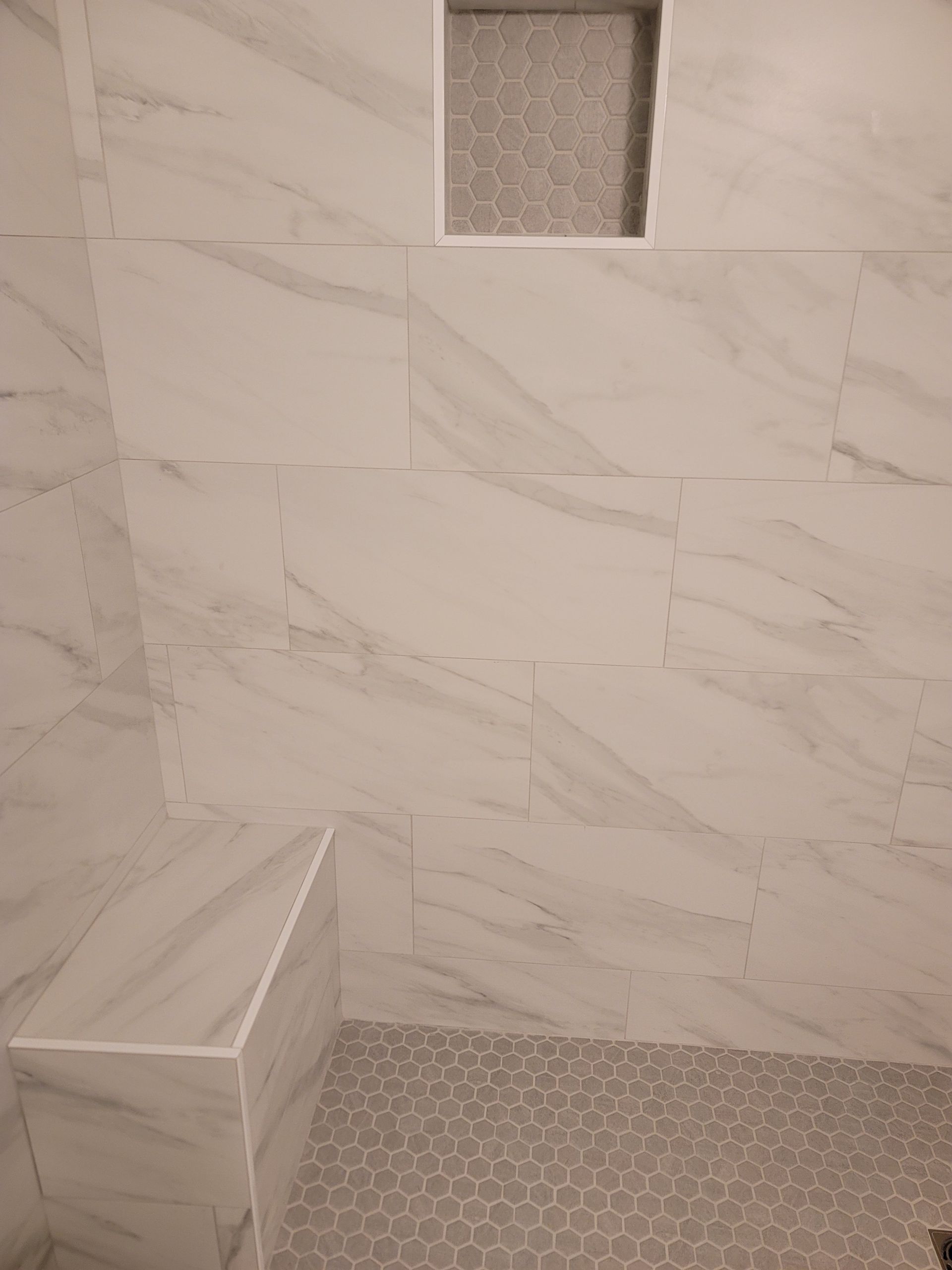 Small tiled shower with marble-look wall tiles, patterned floor, and a recessed shelf niche.