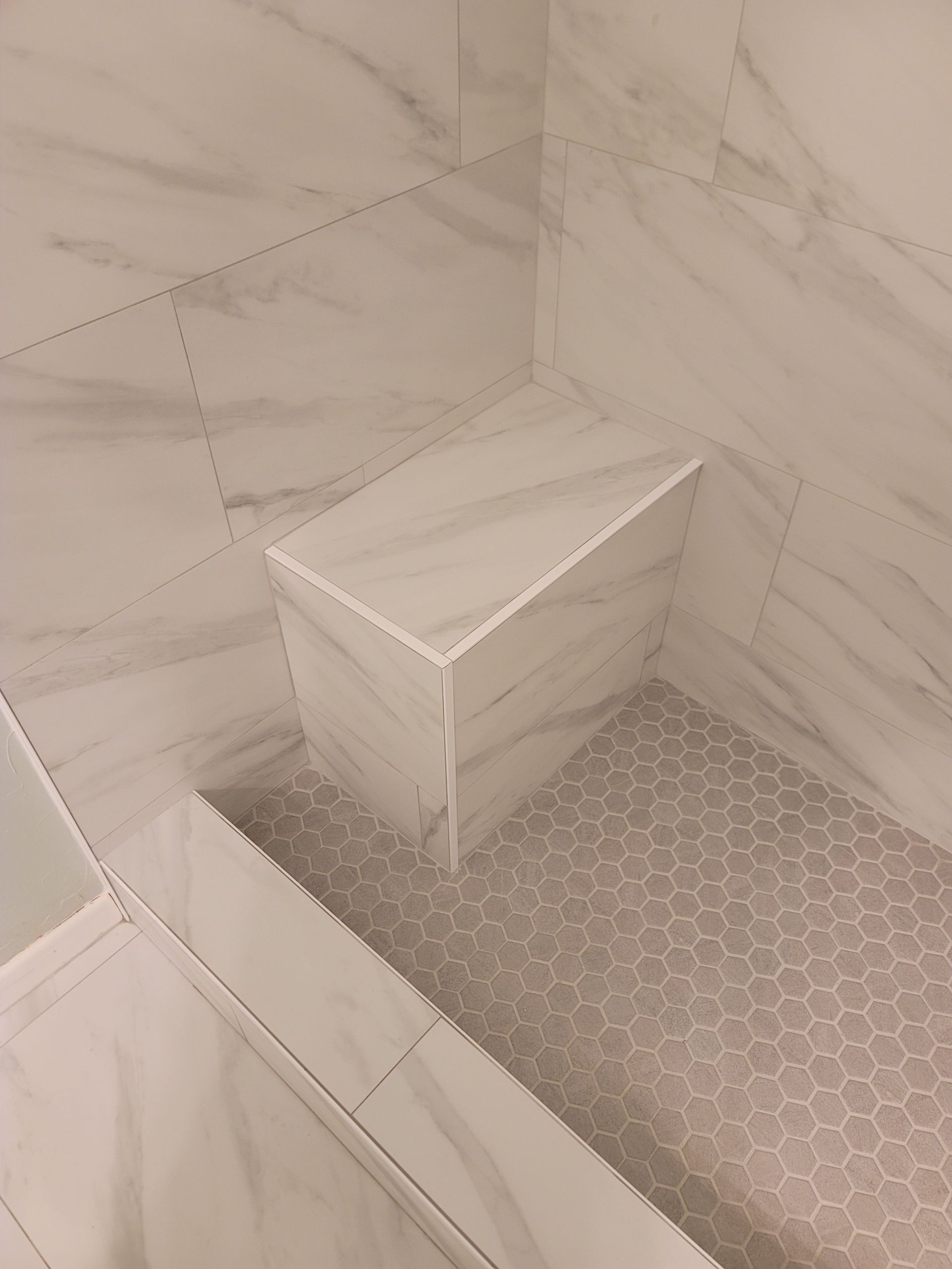 White marble-tile shower corner with a built-in bench and gray hex tile floor