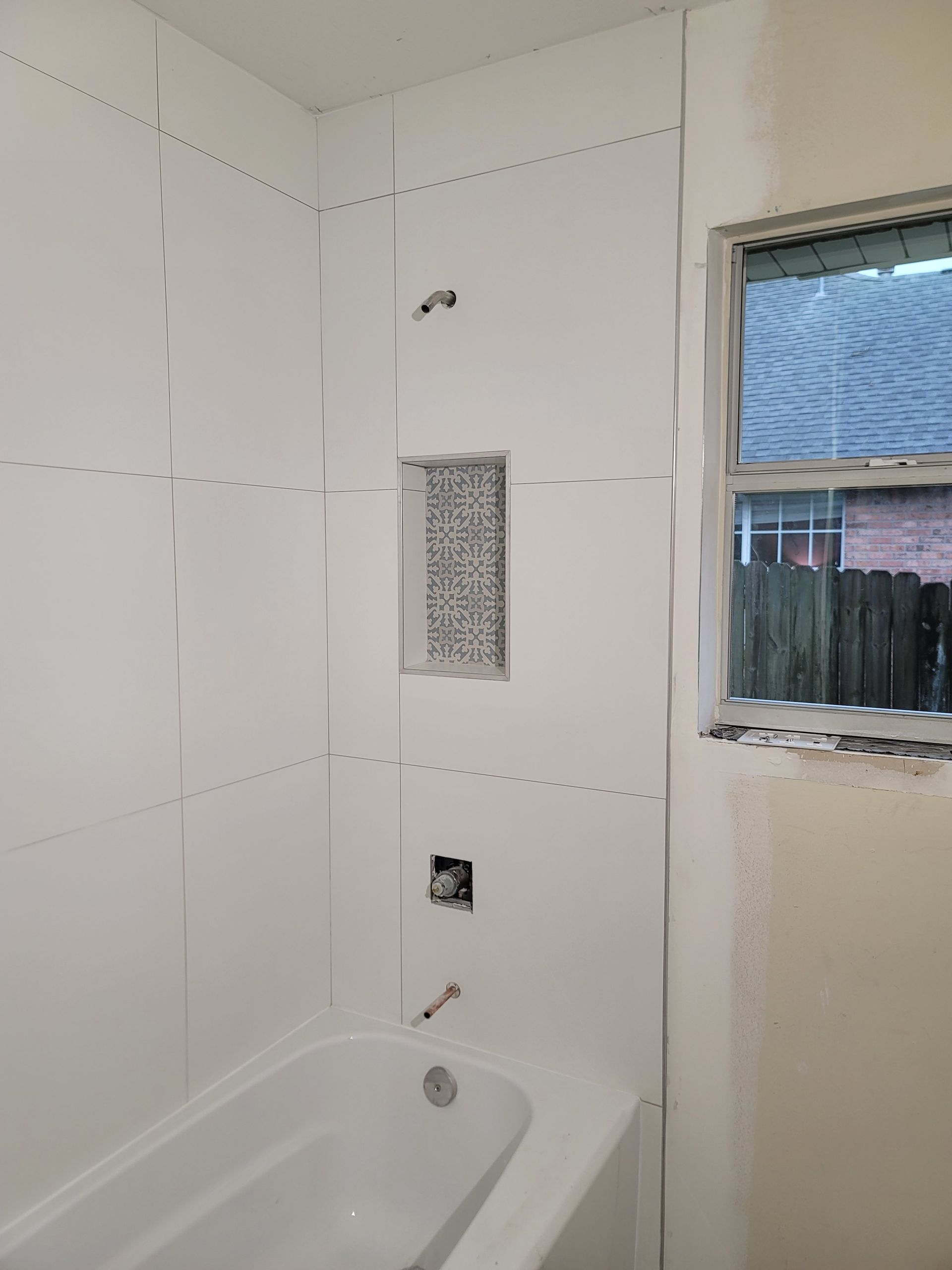 Tiled bathroom wall over a bathtub with a small window and a vent opening.