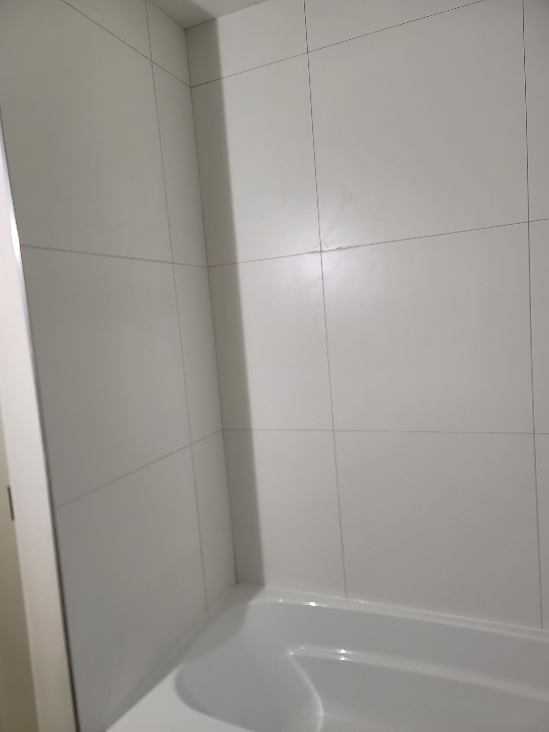 White tiled shower corner with a bathtub edge visible at the bottom.
