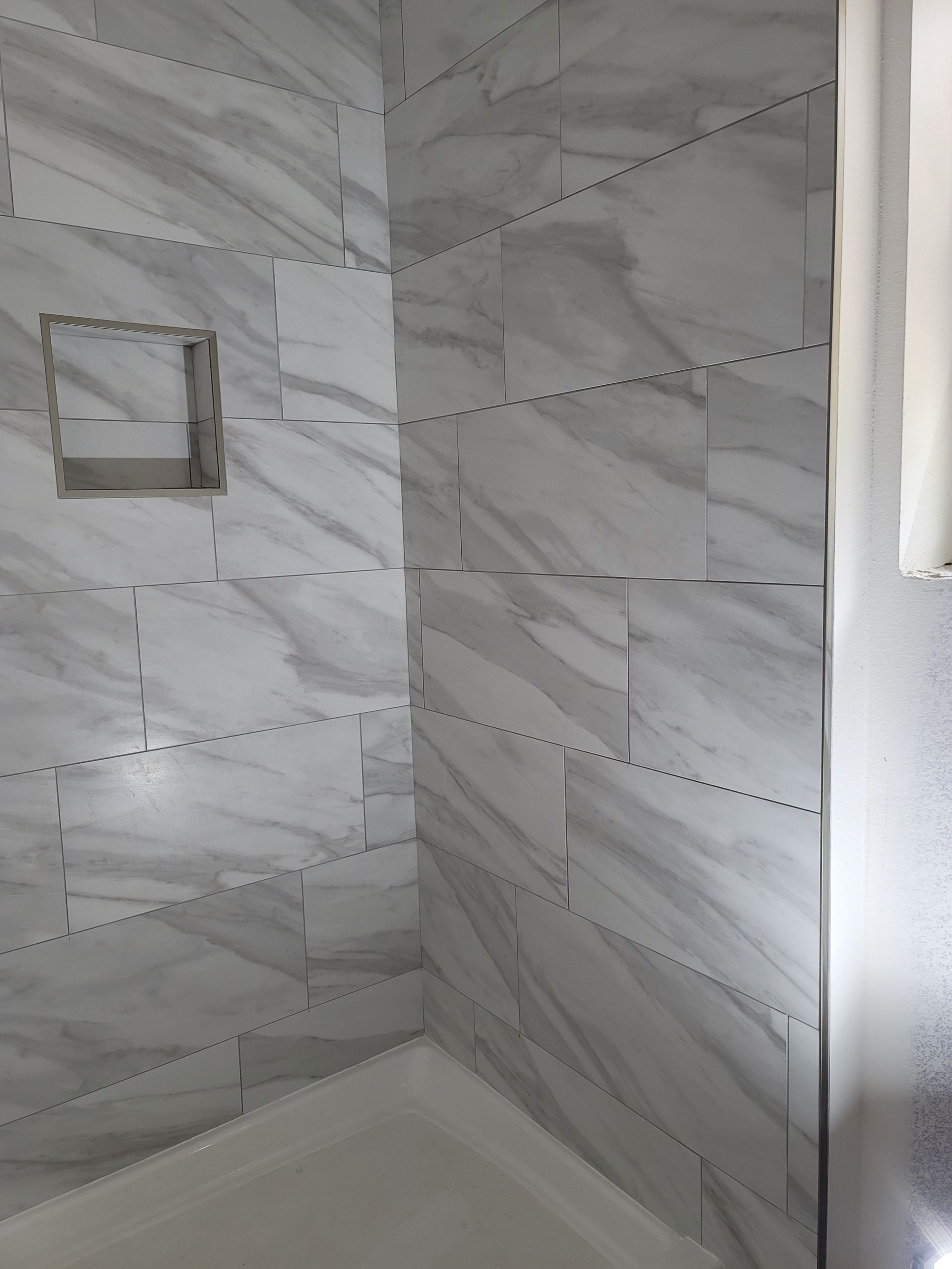 Tiled shower corner with a built-in niche and white marble-look walls.