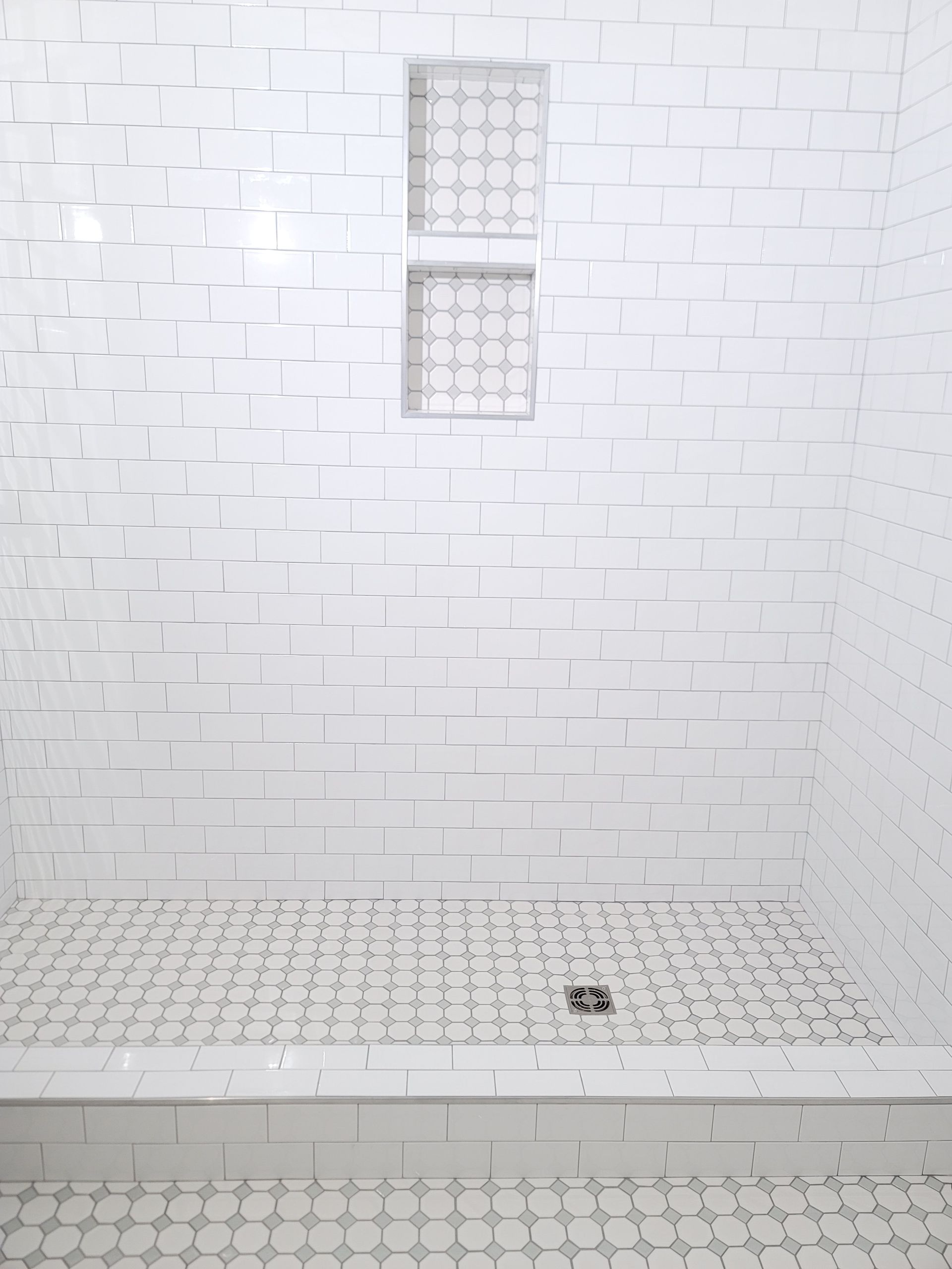 White tiled shower with a built-in shelf and a small floor drain.
