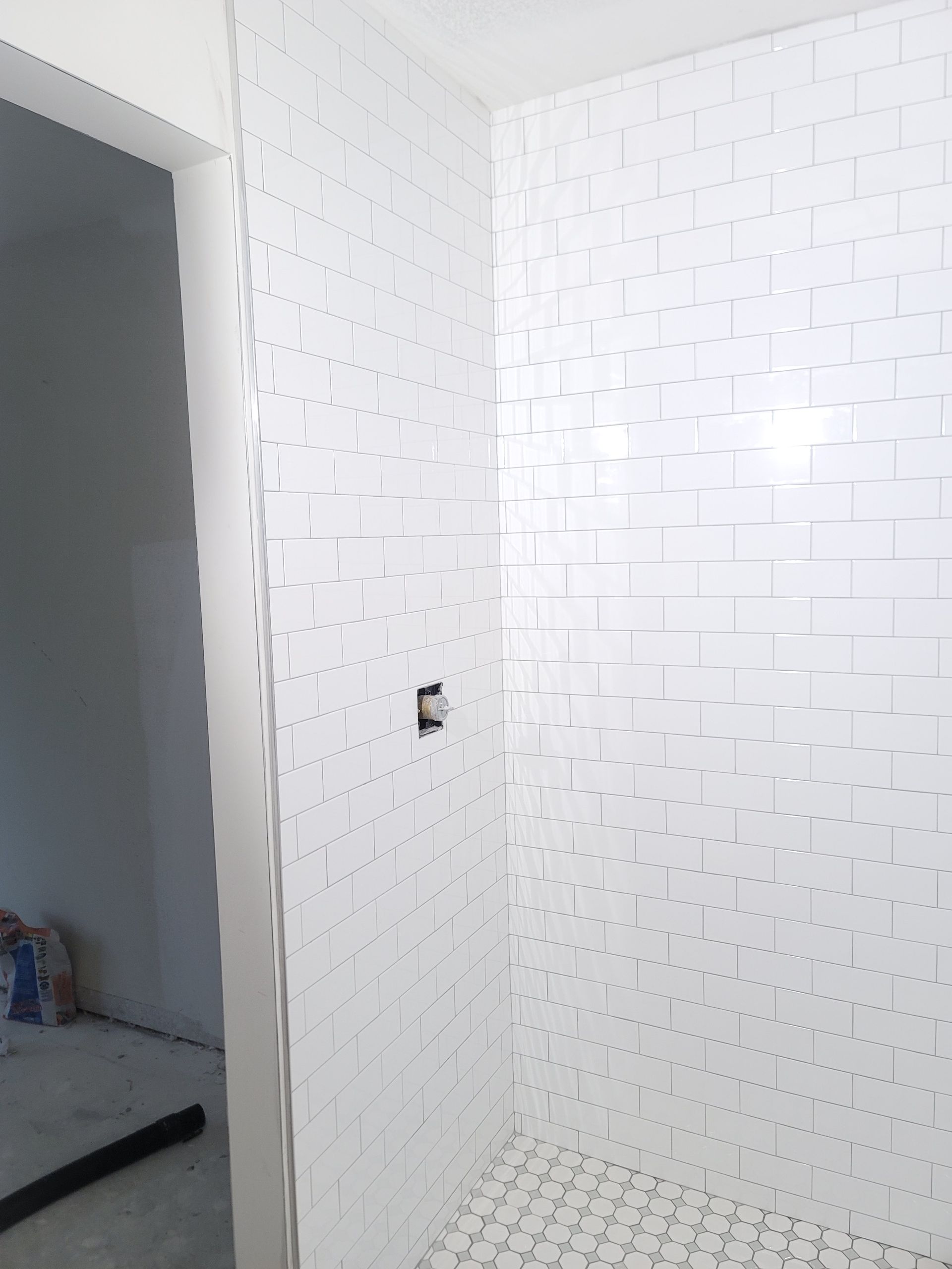 Small white-tiled bathroom or shower area with an open doorway and unfinished wall outlet.