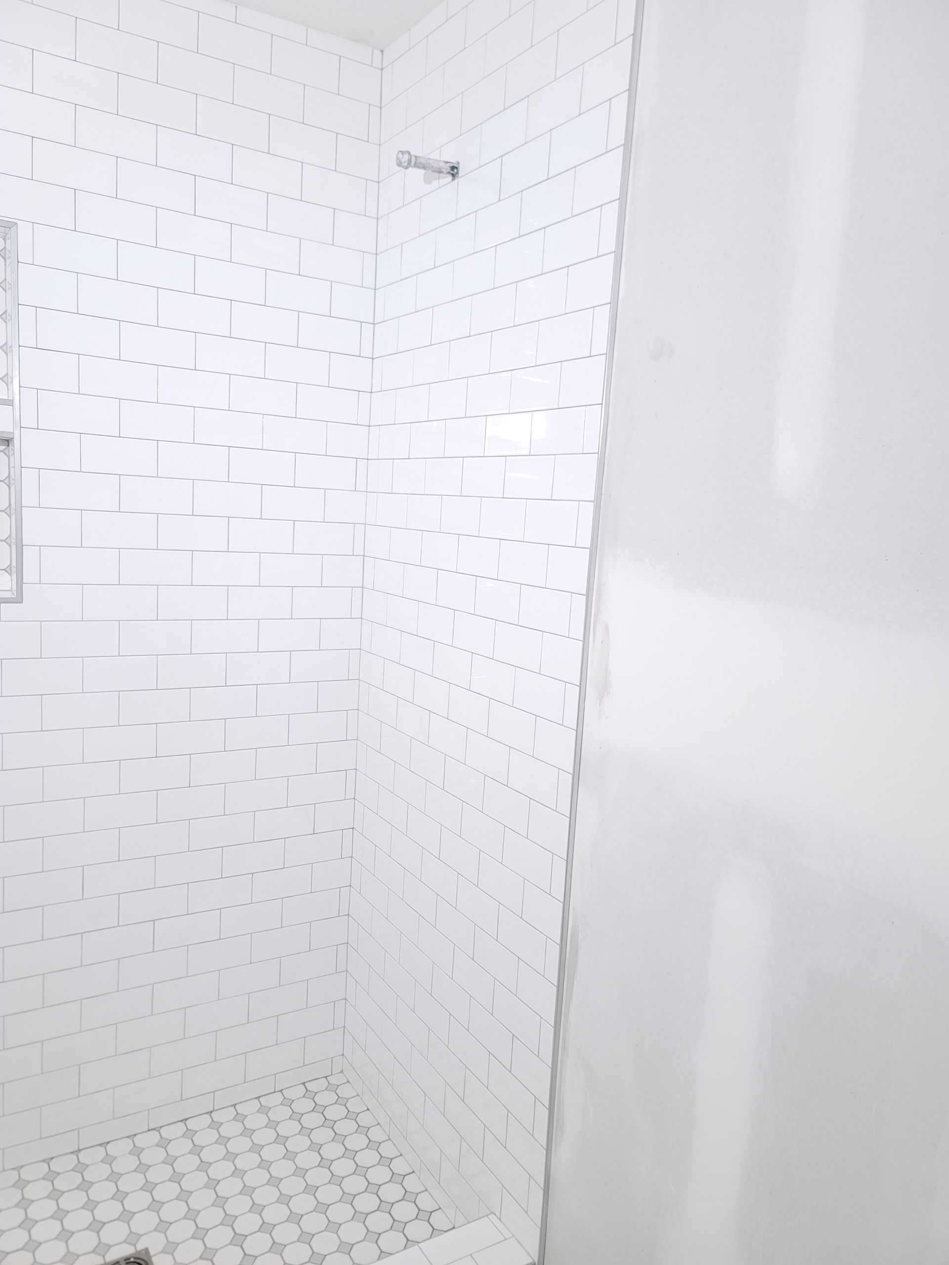 White tiled shower stall with a textured wall and mosaic tile floor
