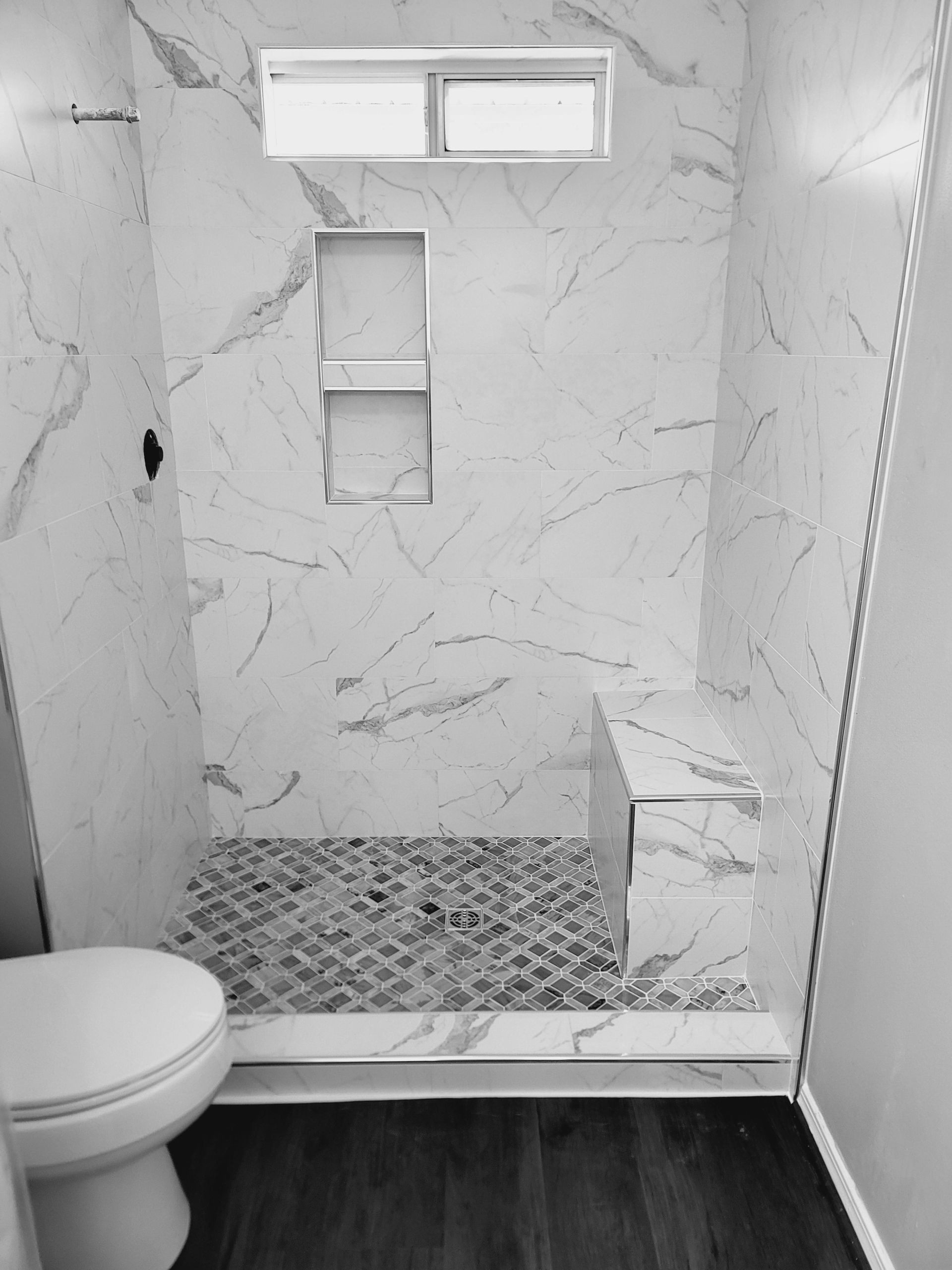 Modern tiled shower with small window, built-in niches, and low bench next to a toilet.