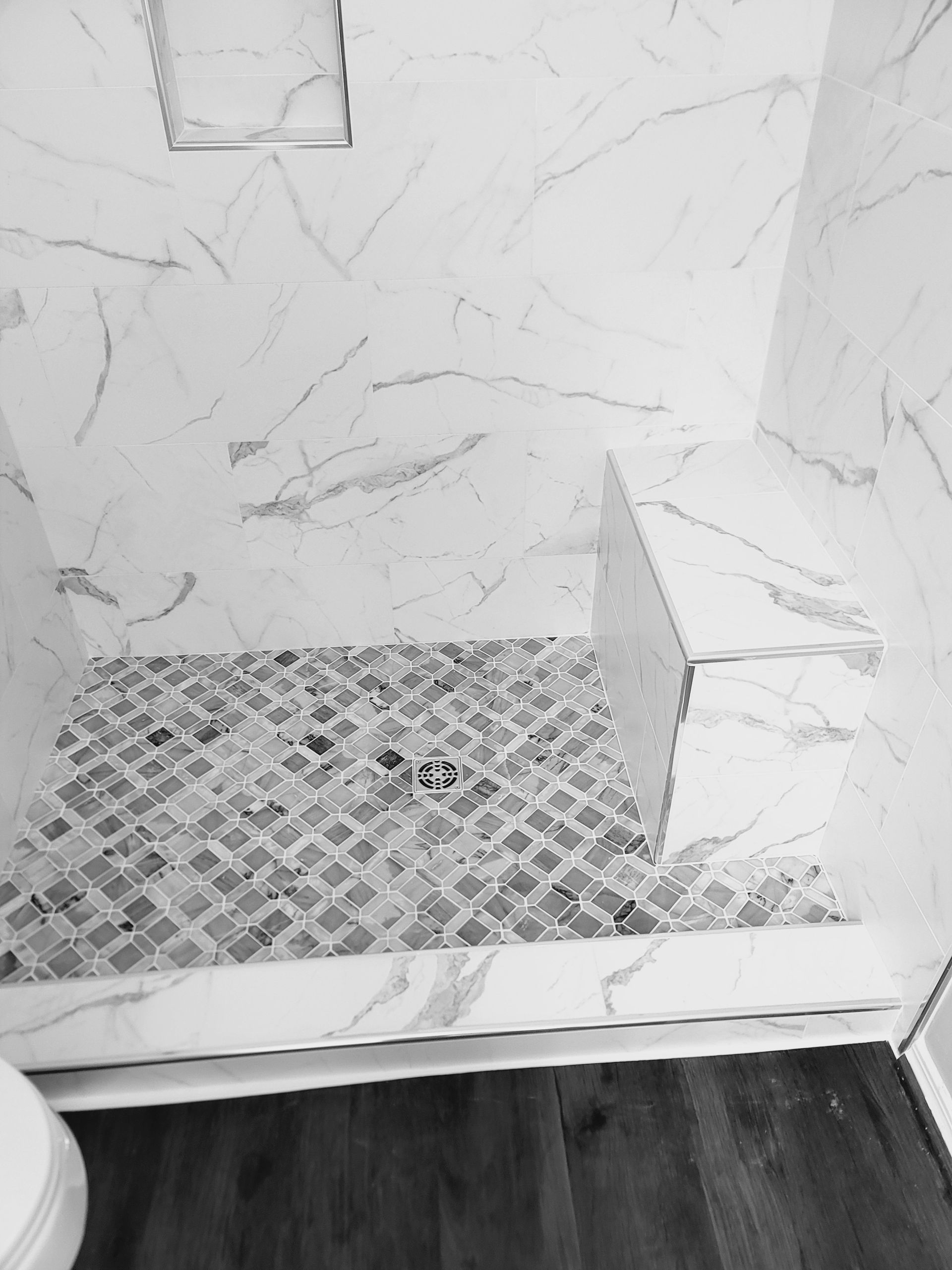 Small tiled shower floor with marble-look wall tiles and a dark wood bathroom floor edge