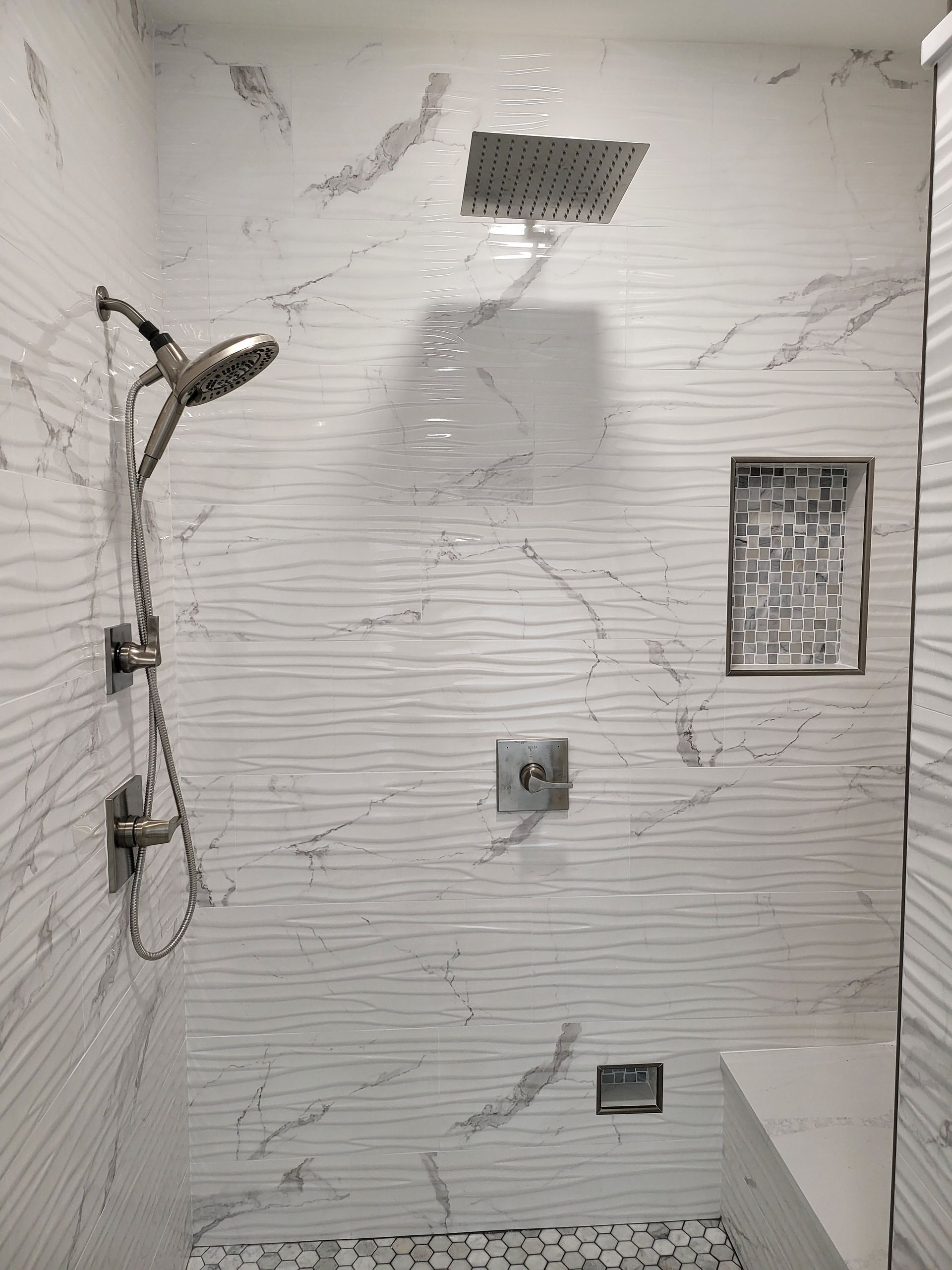 Tiled shower wall with handheld showerhead, built-in shelf, and plumbing fixtures in a bathroom