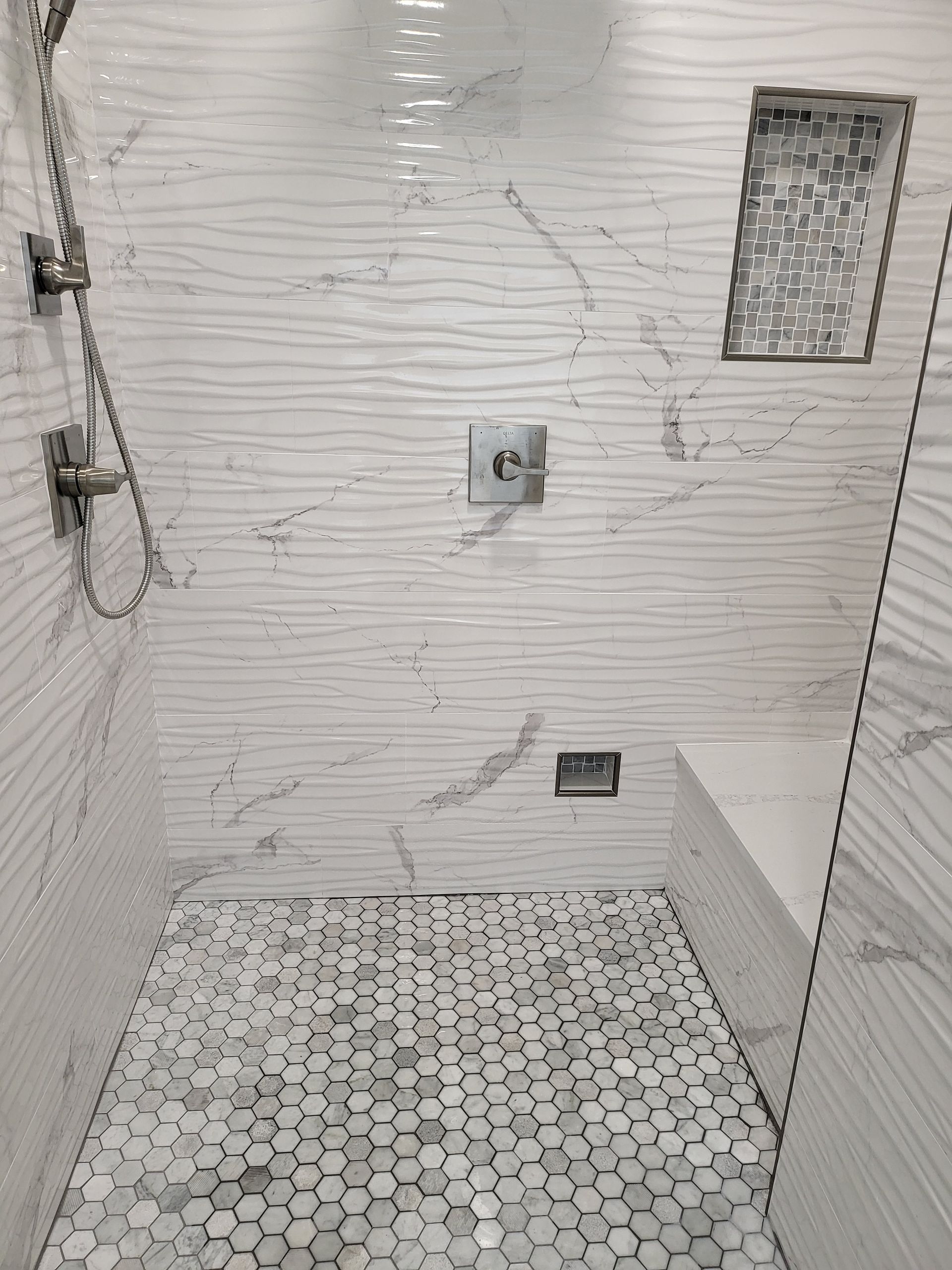White tiled shower with hexagon floor, wall-mounted fixtures, and a small frosted window.