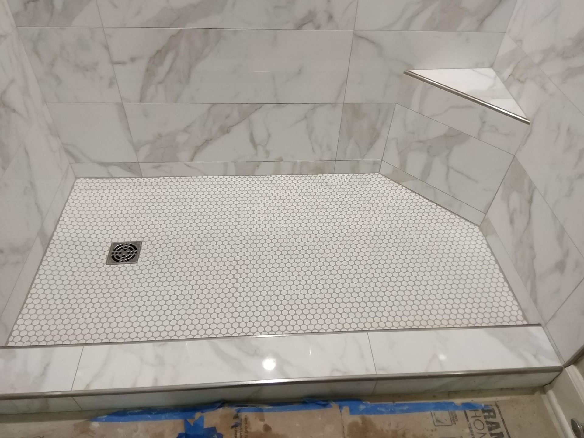 Marble-tiled walk-in shower with pebble floor, bench ledge, and drain