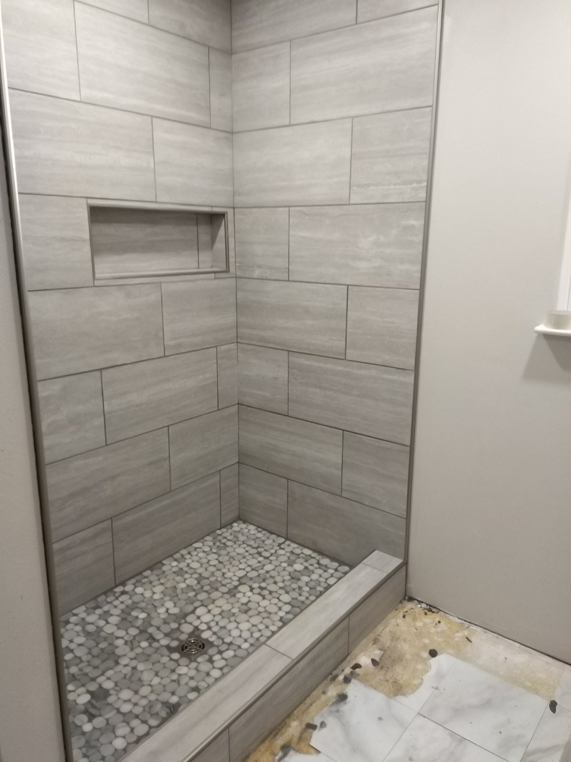 Tiled walk-in shower with a pebble floor and built-in niche, seen during installation.