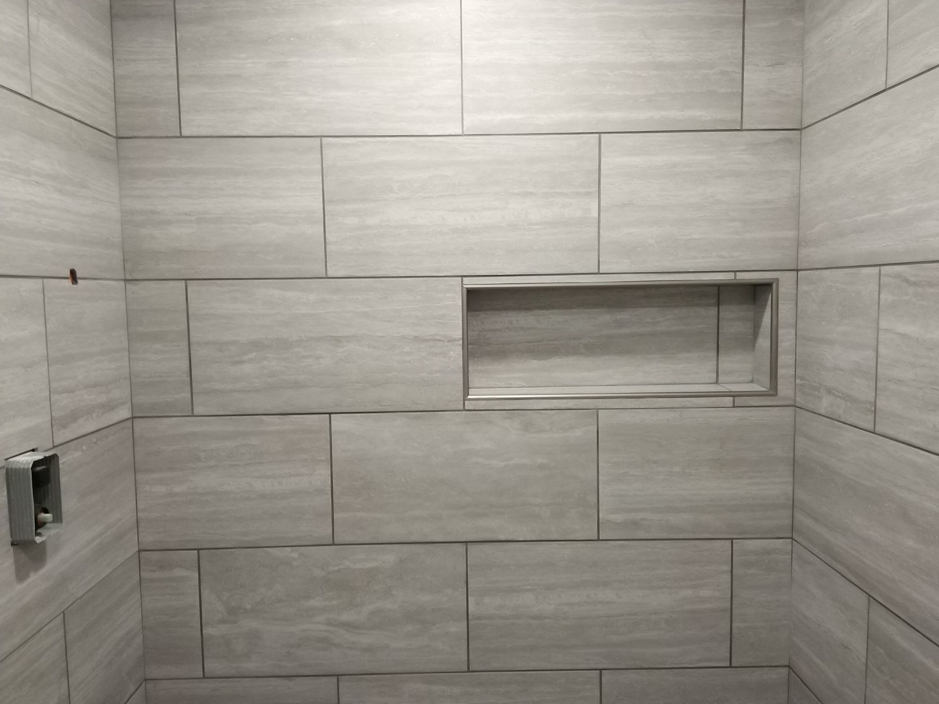 Gray tiled shower wall with a recessed niche and built-in soap holder