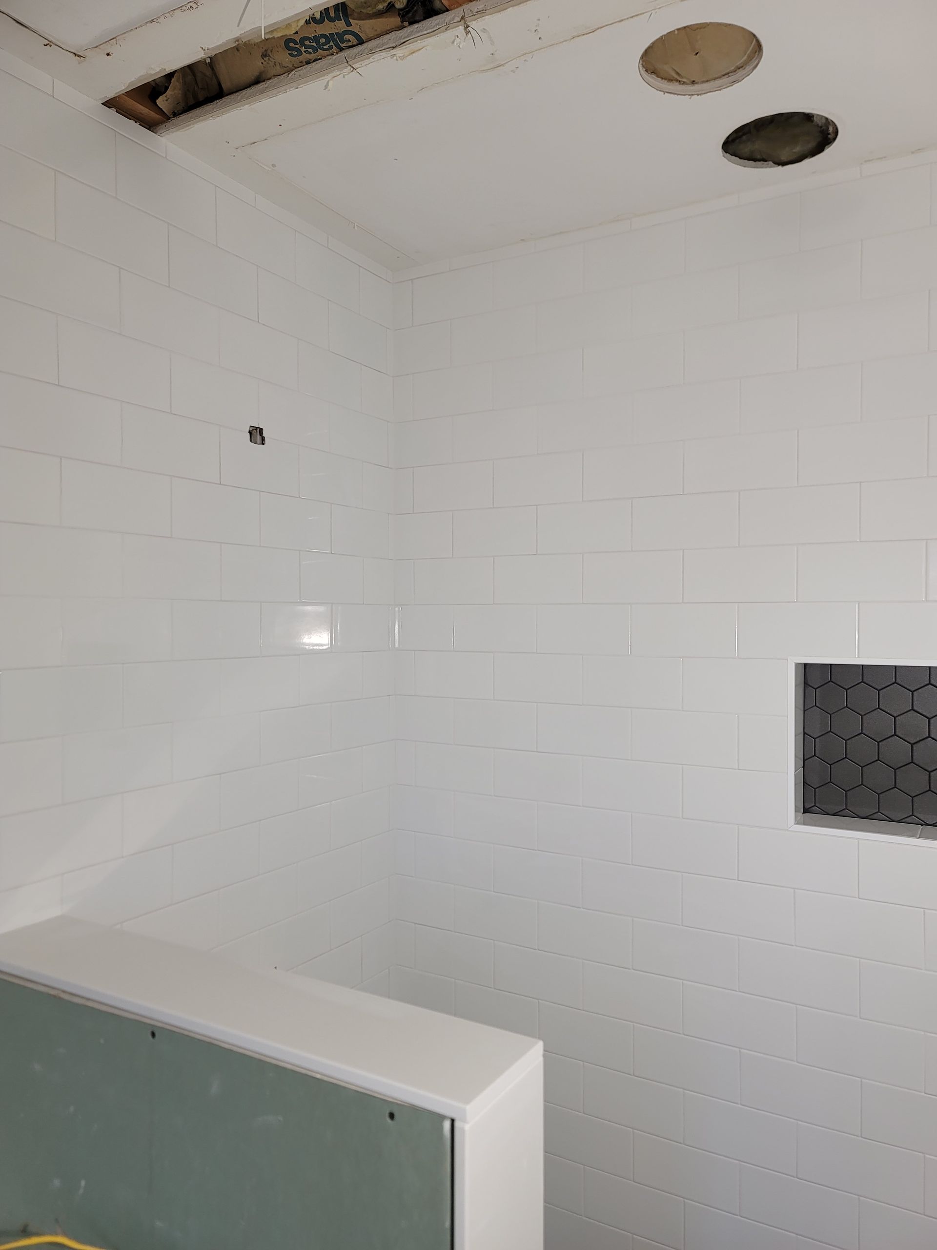 Empty white tiled shower room with damaged ceiling and a half-height partition in the foreground
