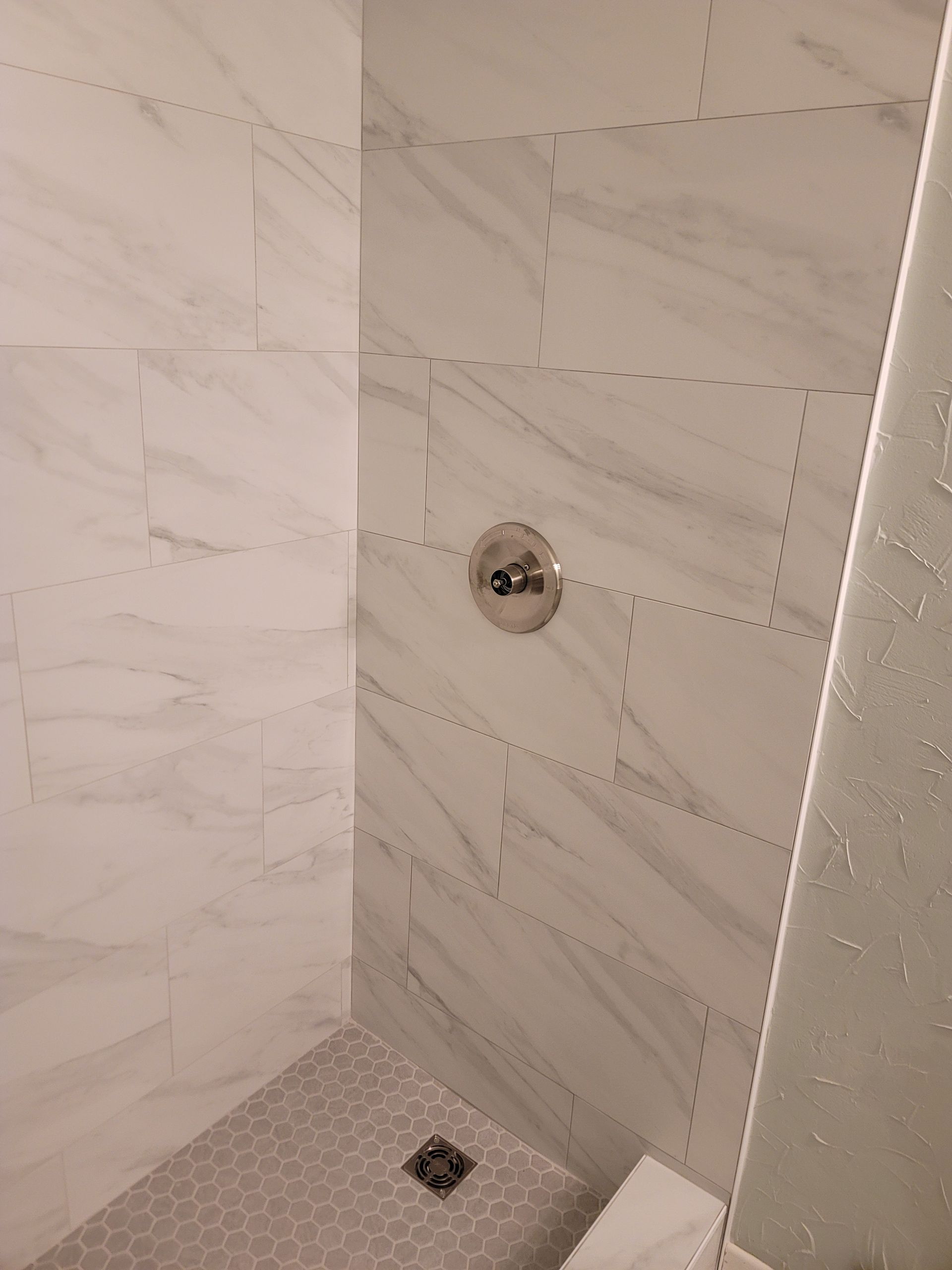 Empty tiled shower corner with wall-mounted faucet and drain.