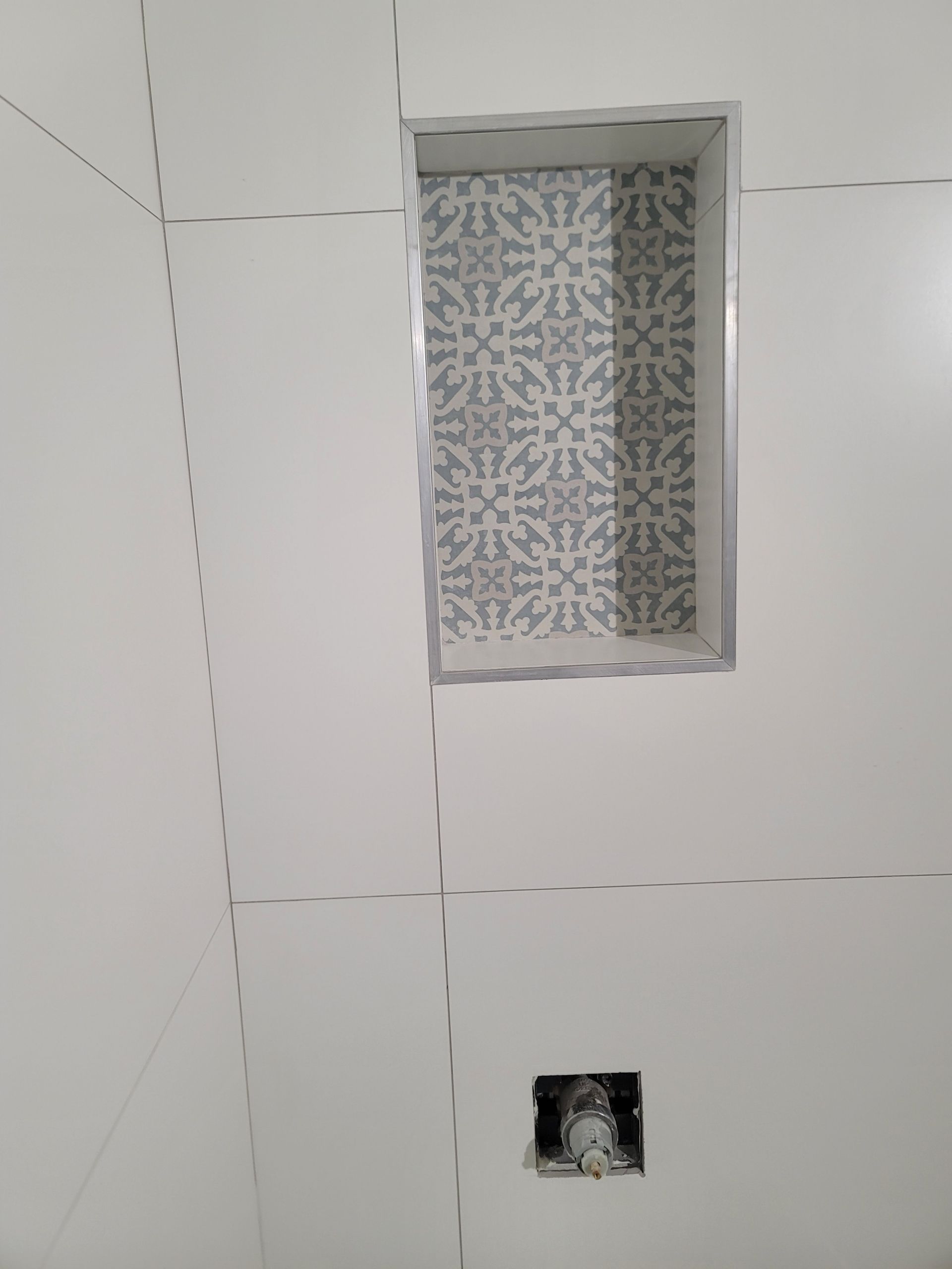 Tiled bathroom wall with a small frosted window and exposed plumbing outlet near the floor