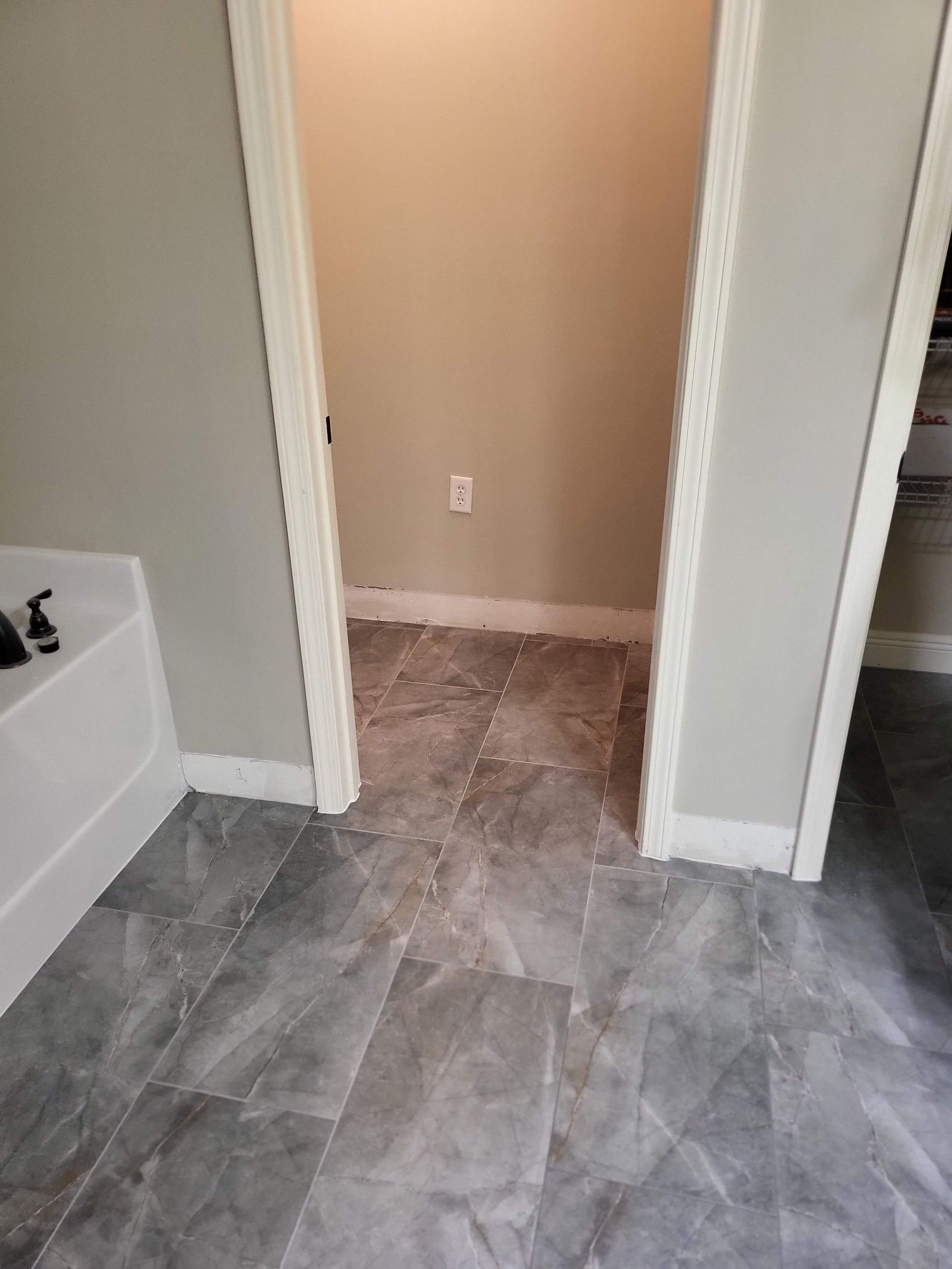 Hallway with gray tile floor, beige walls, and an open doorway leading to a small room.