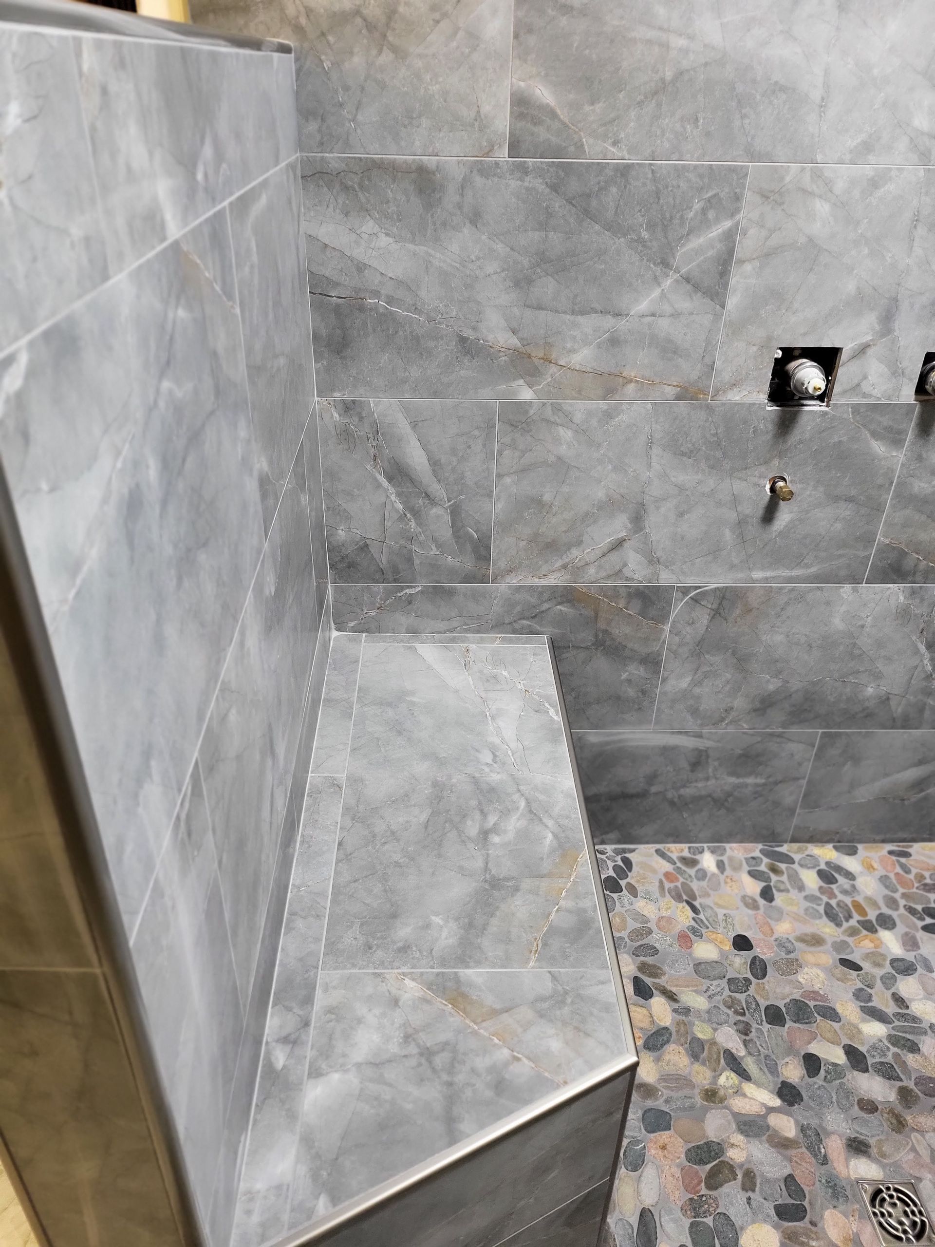 Gray tiled shower corner with a built-in bench and mosaic floor.