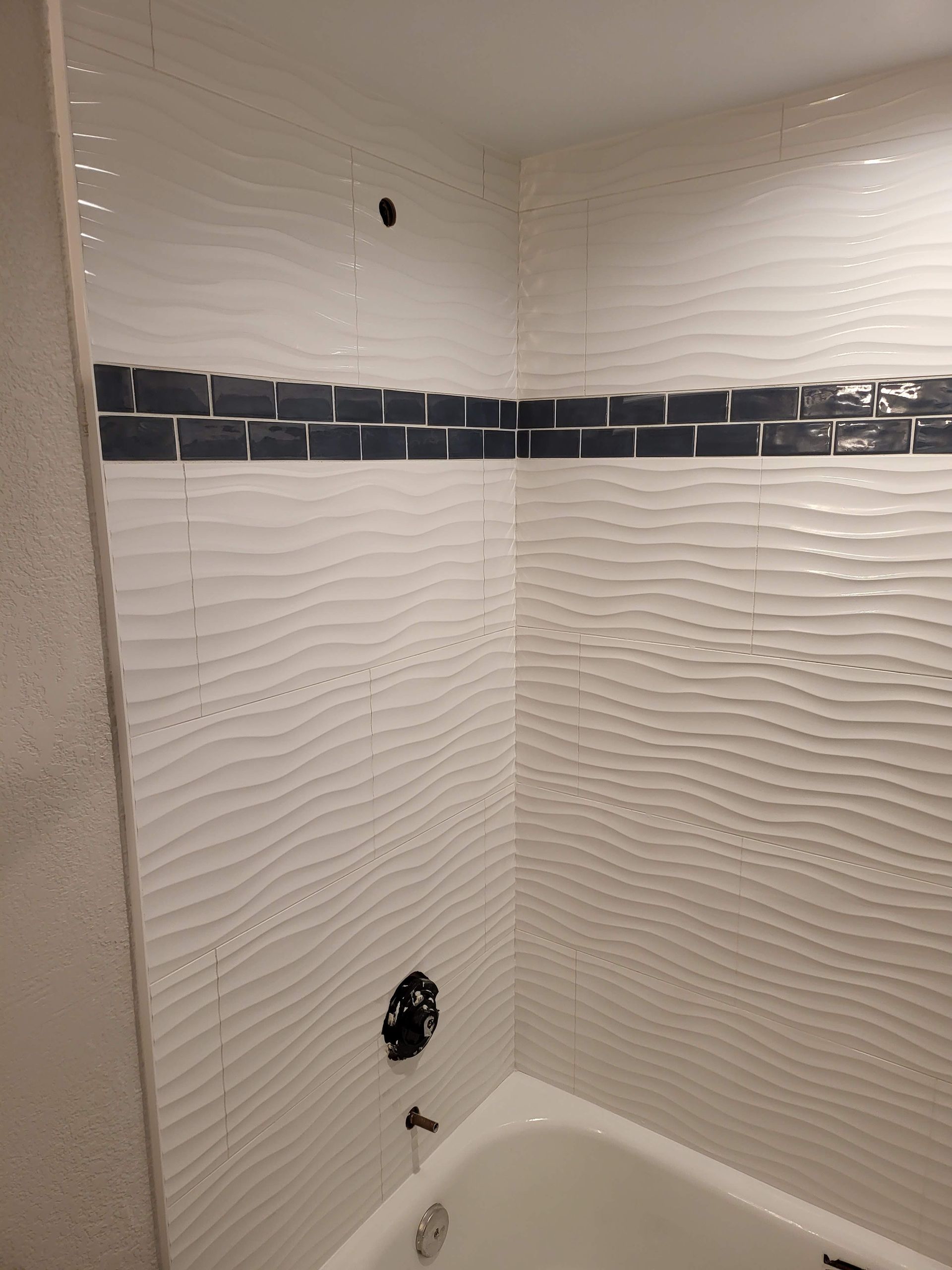 Tiled shower alcove with white wavy walls, dark accent border, and plumbing fixtures installed