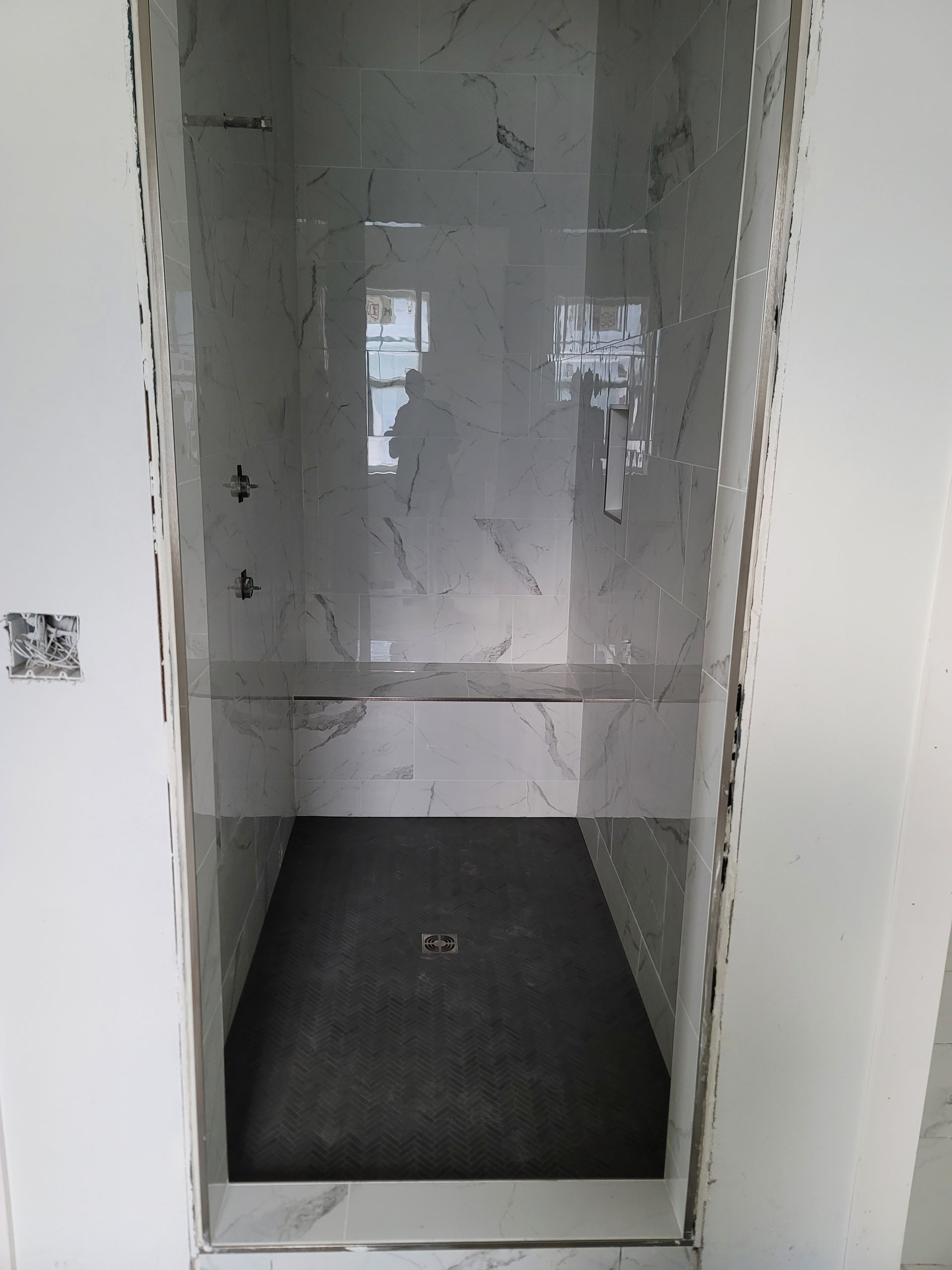 Empty recessed shower stall with white tiled walls and a dark floor mat.