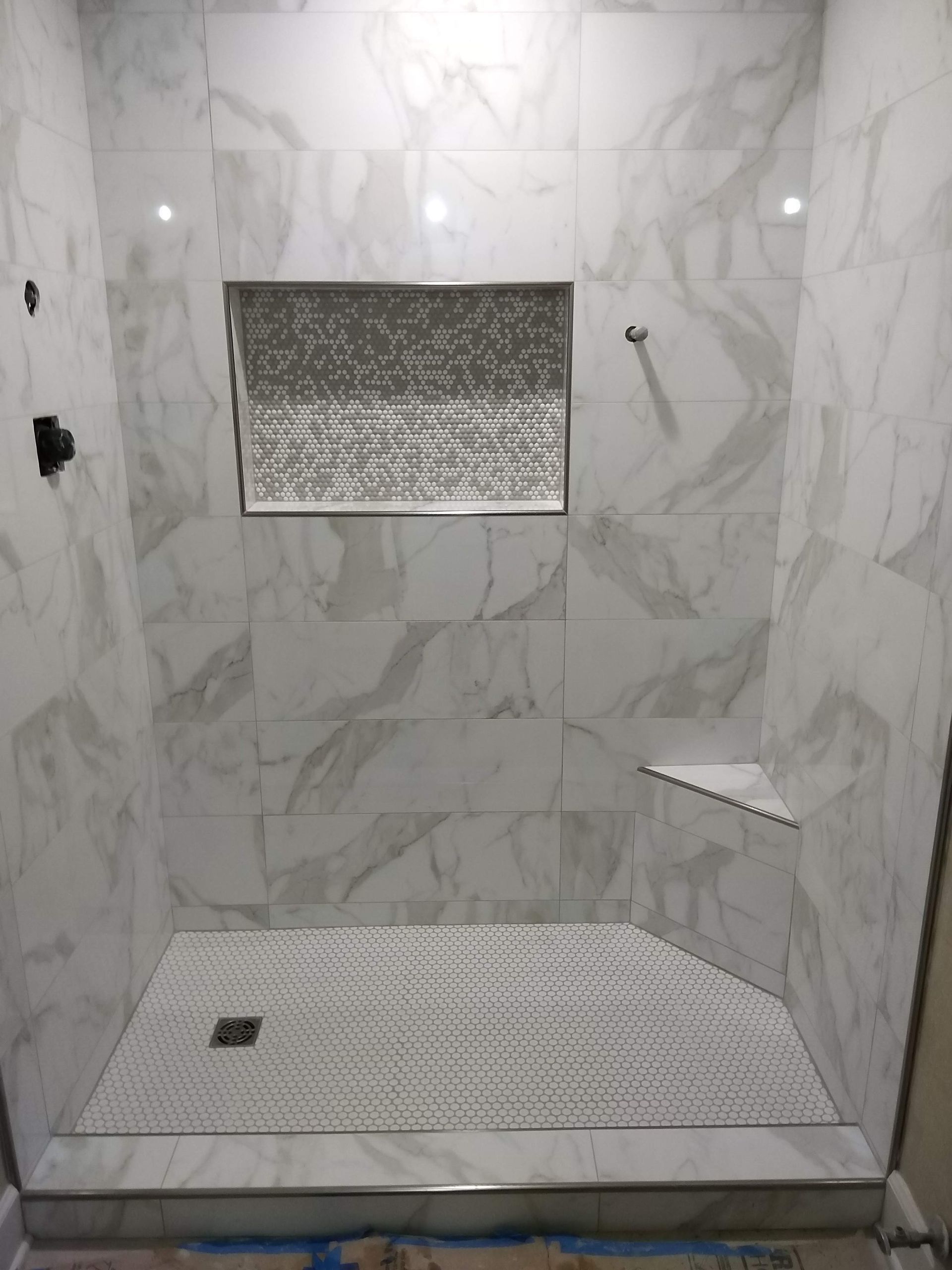 Marble-tiled walk-in shower with bench, niche, corner shelf, and tiled floor drain.