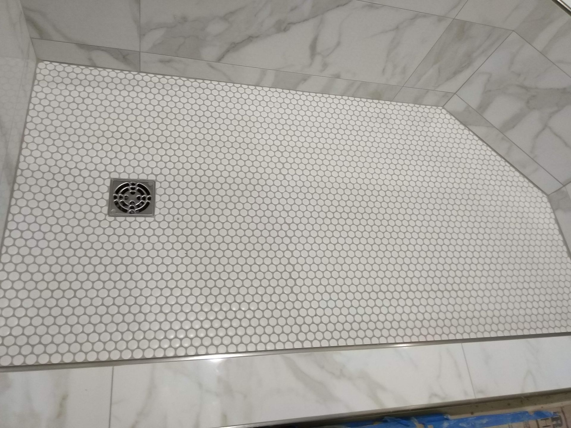 Hex-tile shower floor with a square drain in a white marble bathroom.