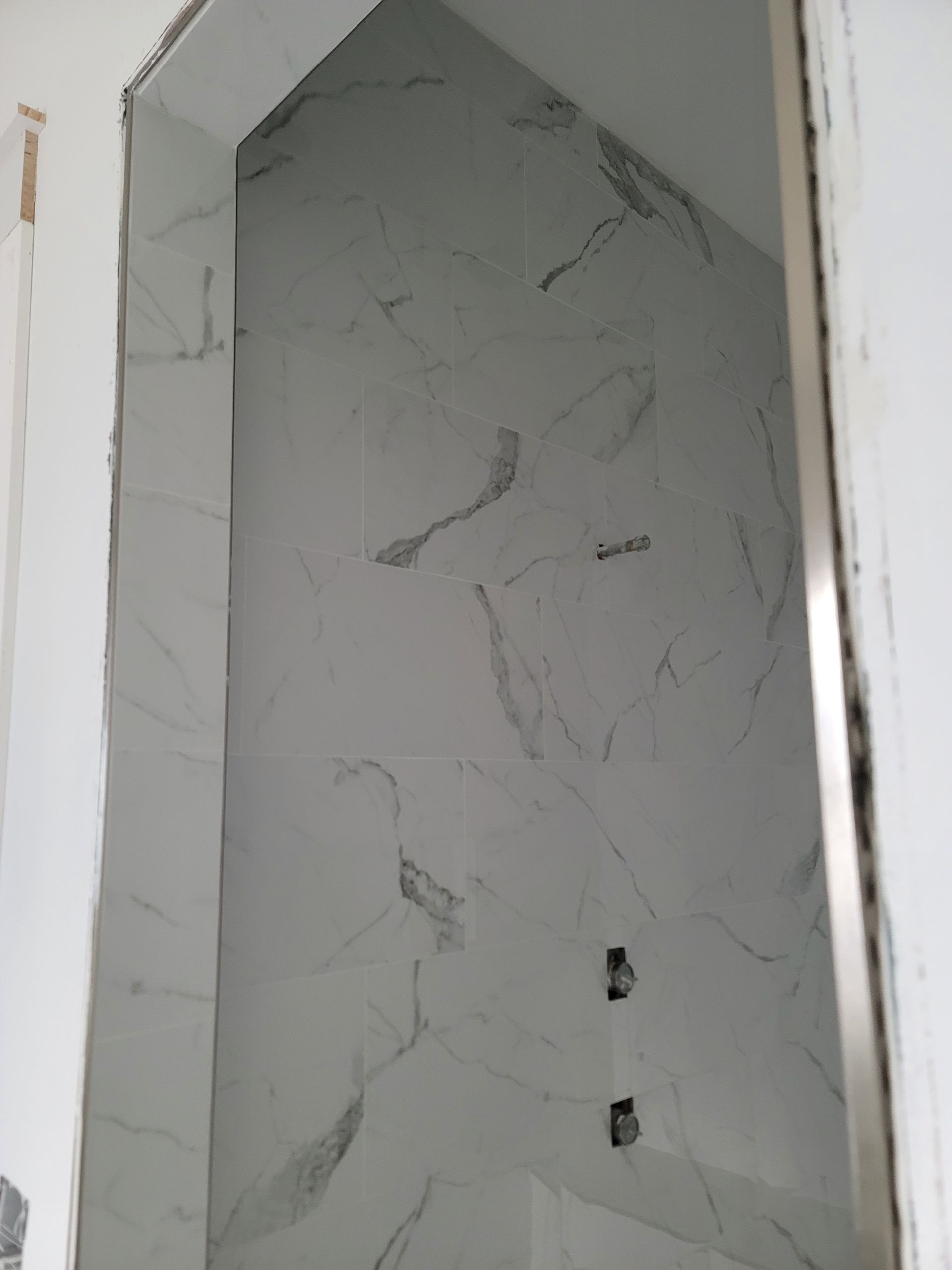 Marble-look tiled shower niche with two plumbing openings in a white wall