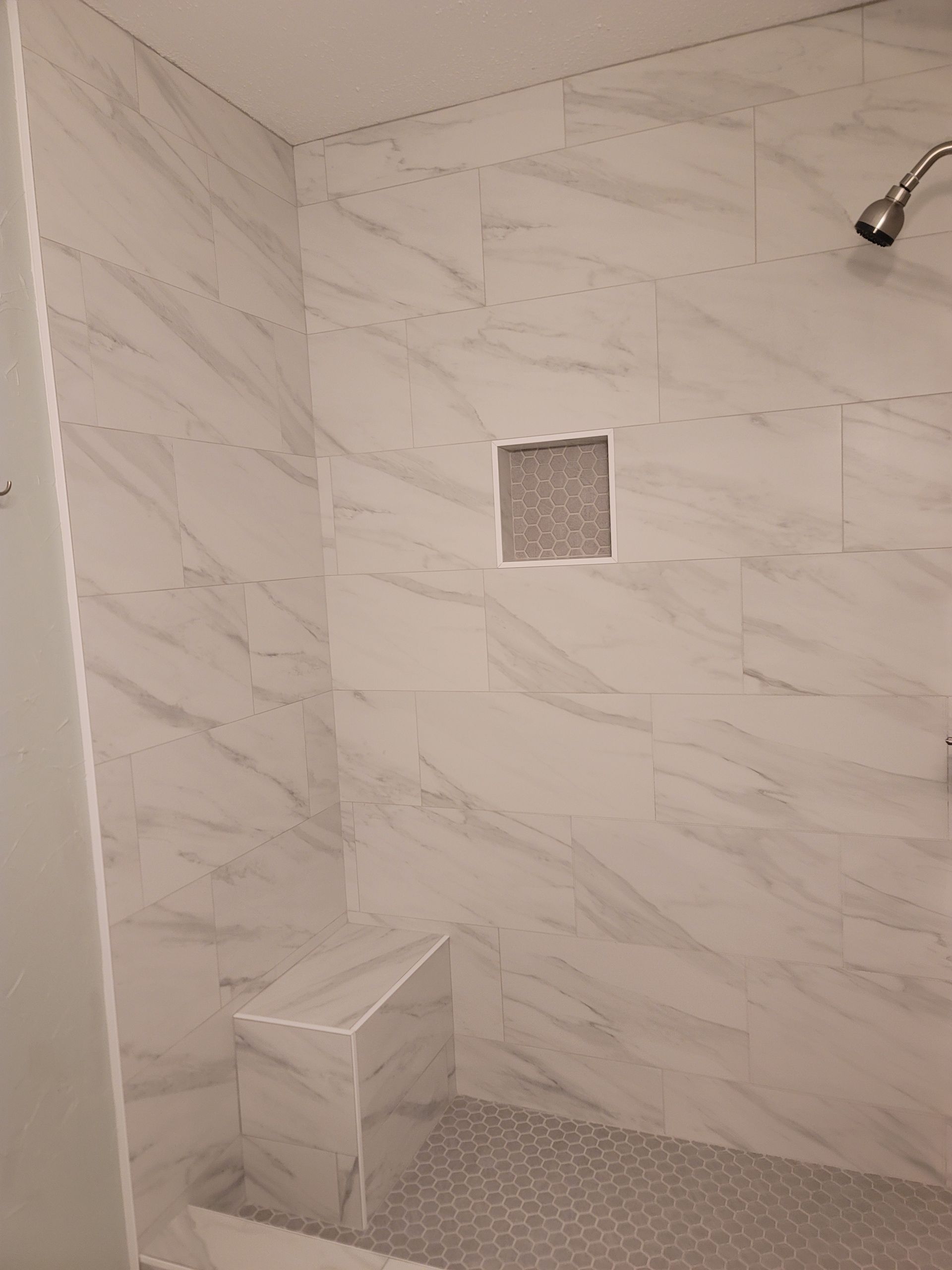 Empty tiled shower with a small seat, square wall niche, and chrome showerhead.