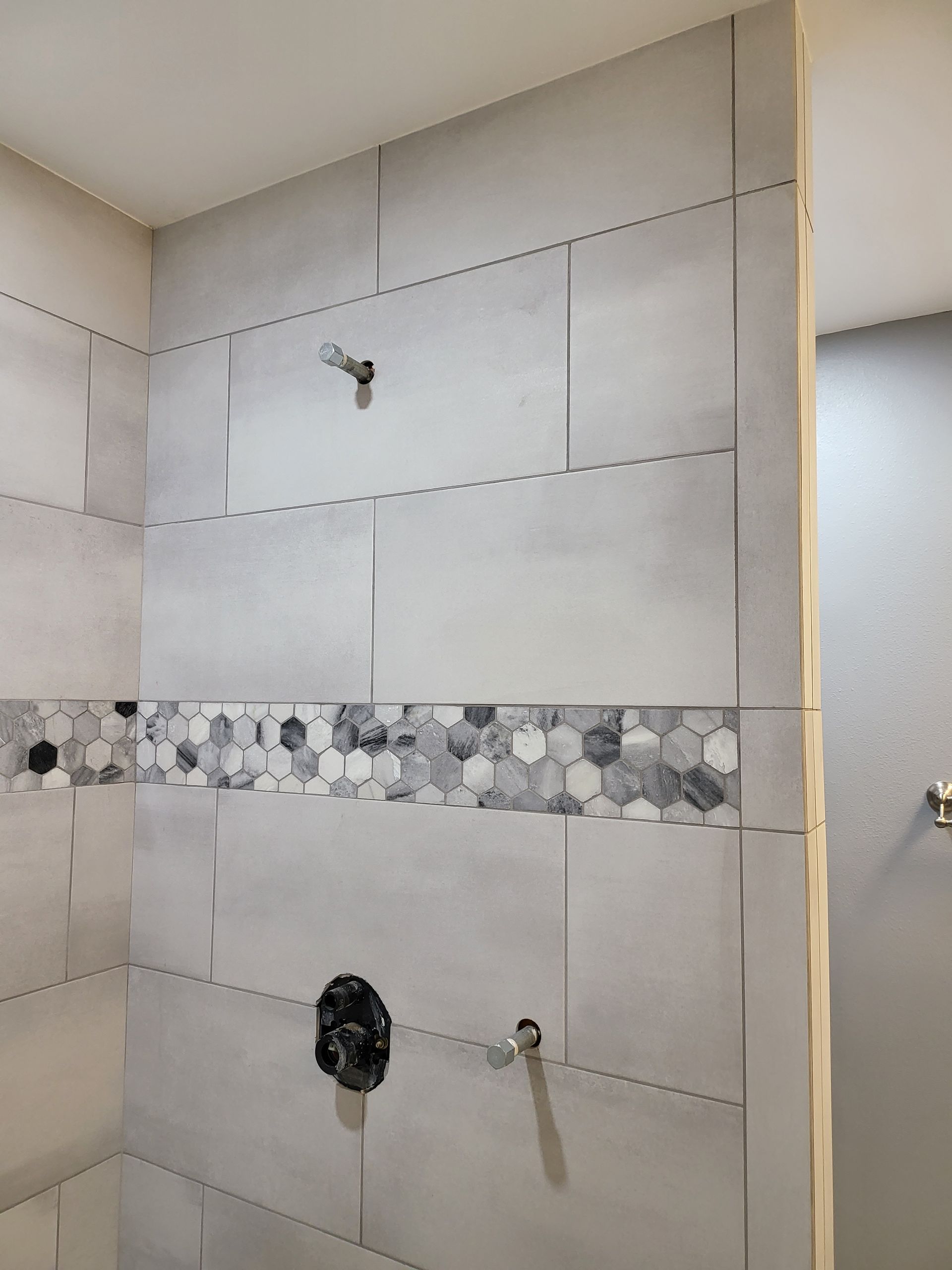 Tiled shower wall with gray tiles, a decorative stone strip, and shower fixtures cutouts
