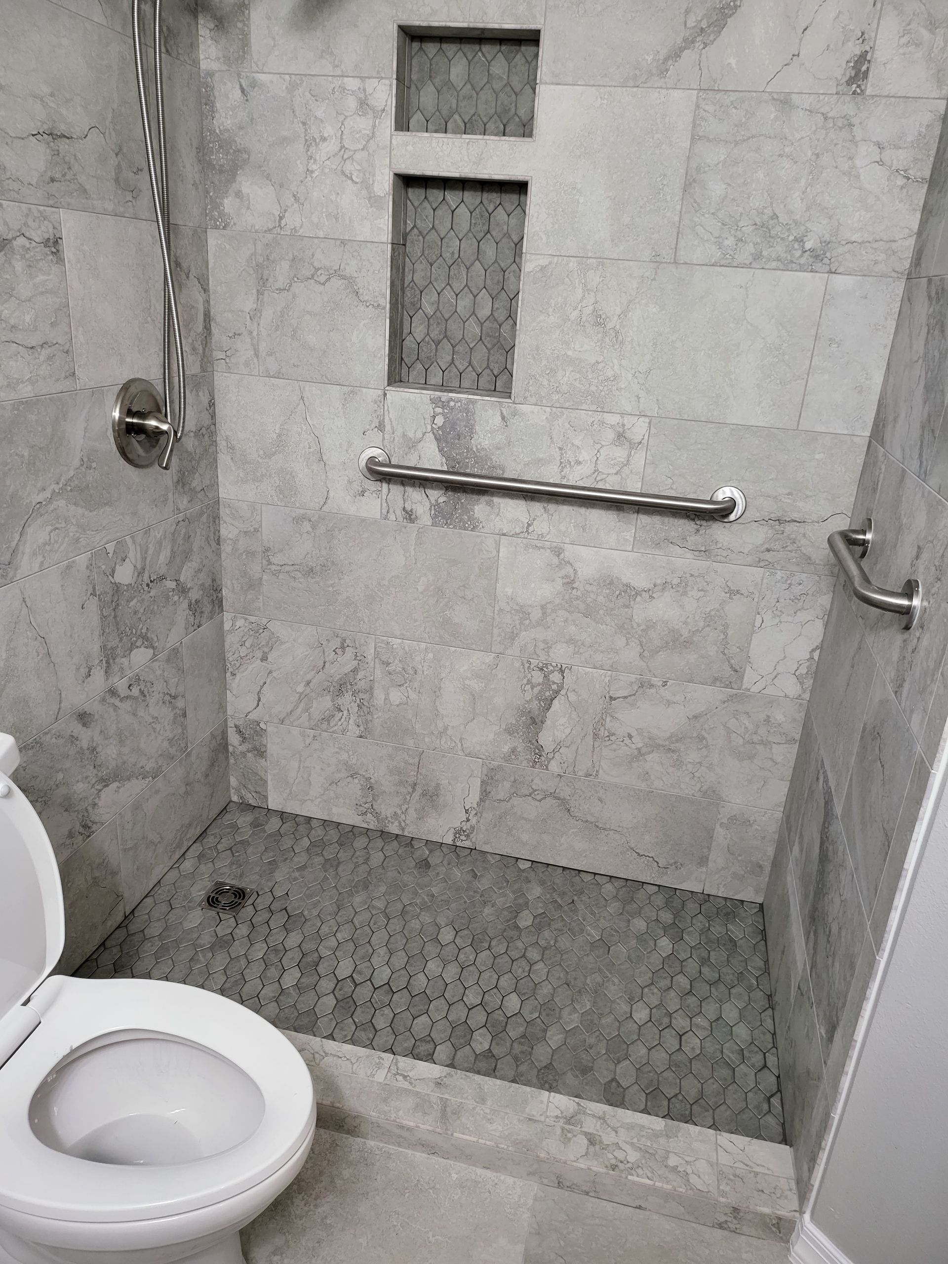 Small tiled bathroom shower area with a grab bar, built-in niches, and a toilet in the foreground.