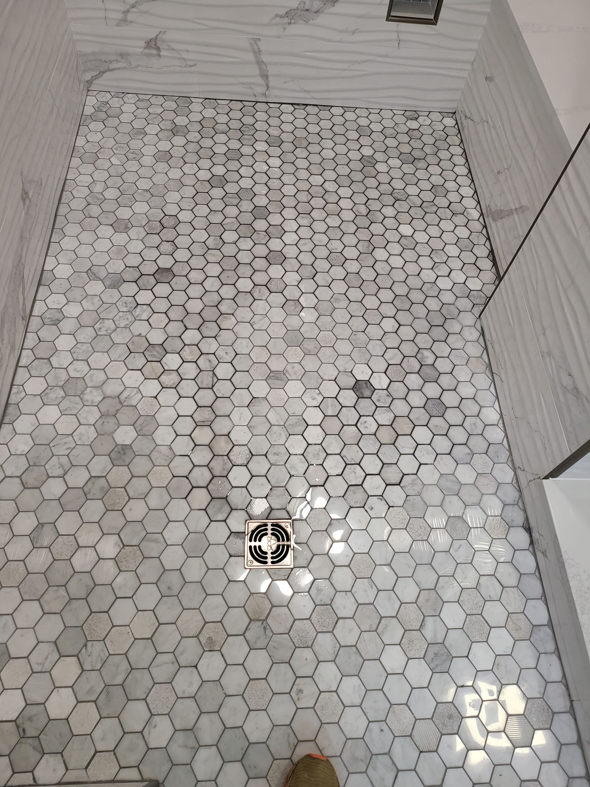 Small bathroom with hexagon-tile floor and shower wall, viewed from above.