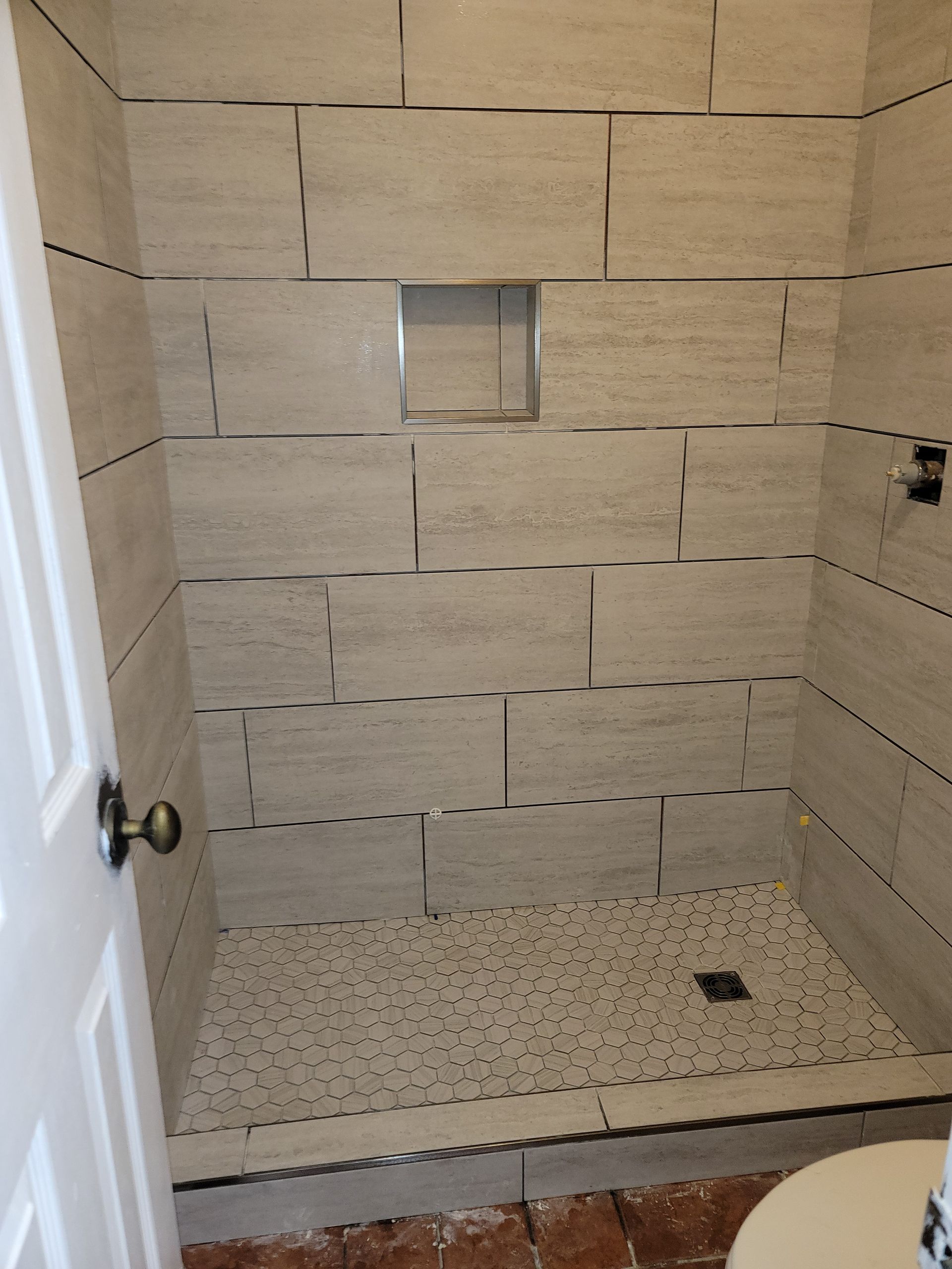 Empty tiled walk-in shower with a bench niche and pebble-style floor.