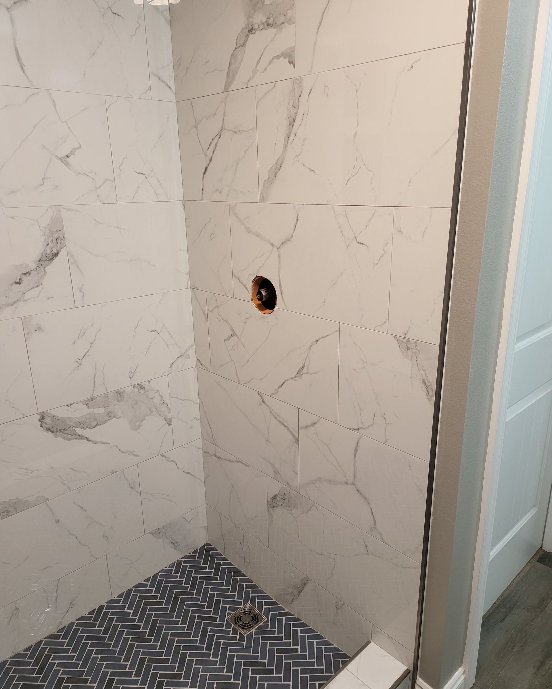 Tiled shower wall with a small hole exposing wiring or plumbing near the center.