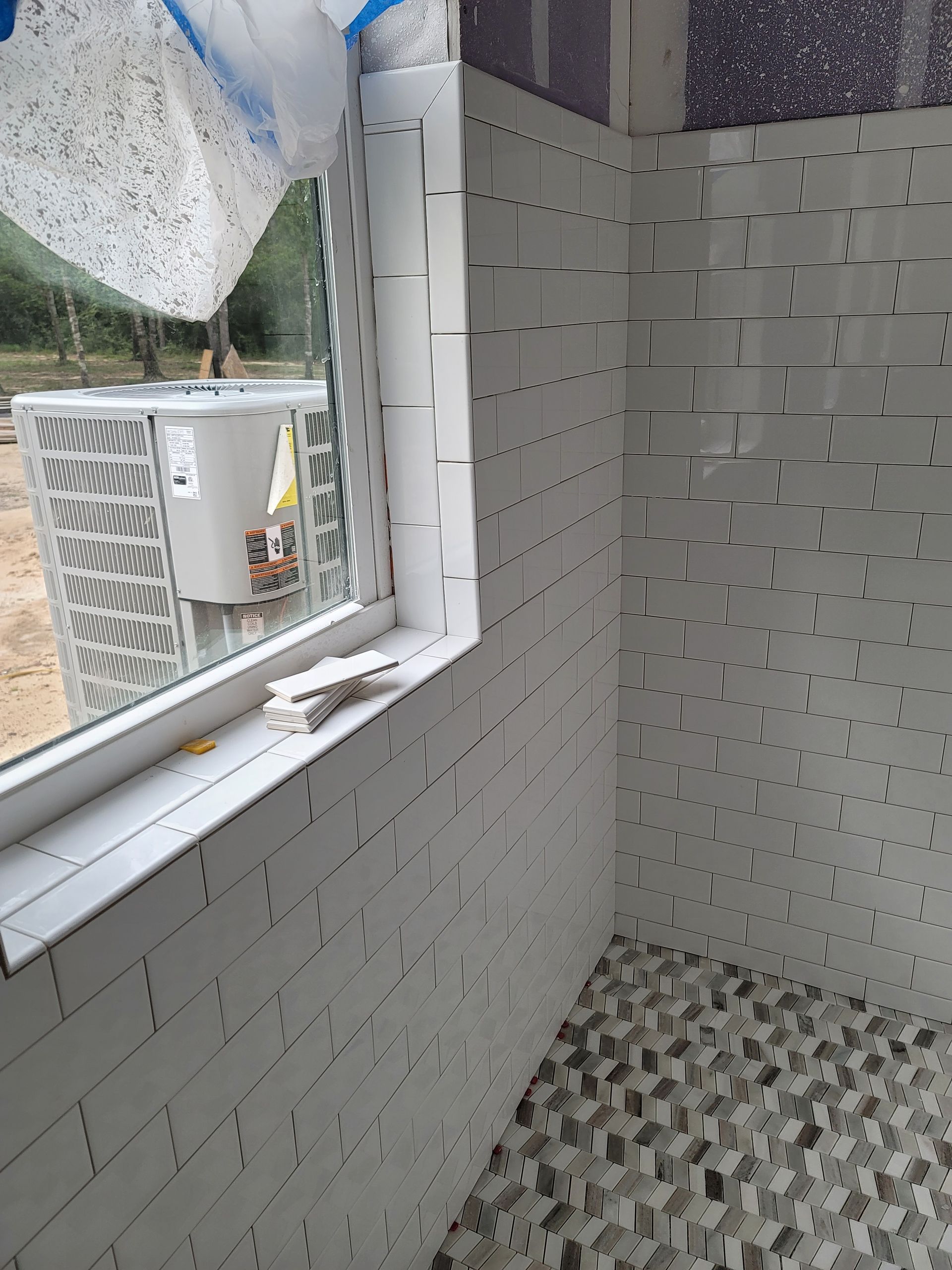 Interior of a small tiled room with an open window and air conditioner outside, showing a checkered floor.